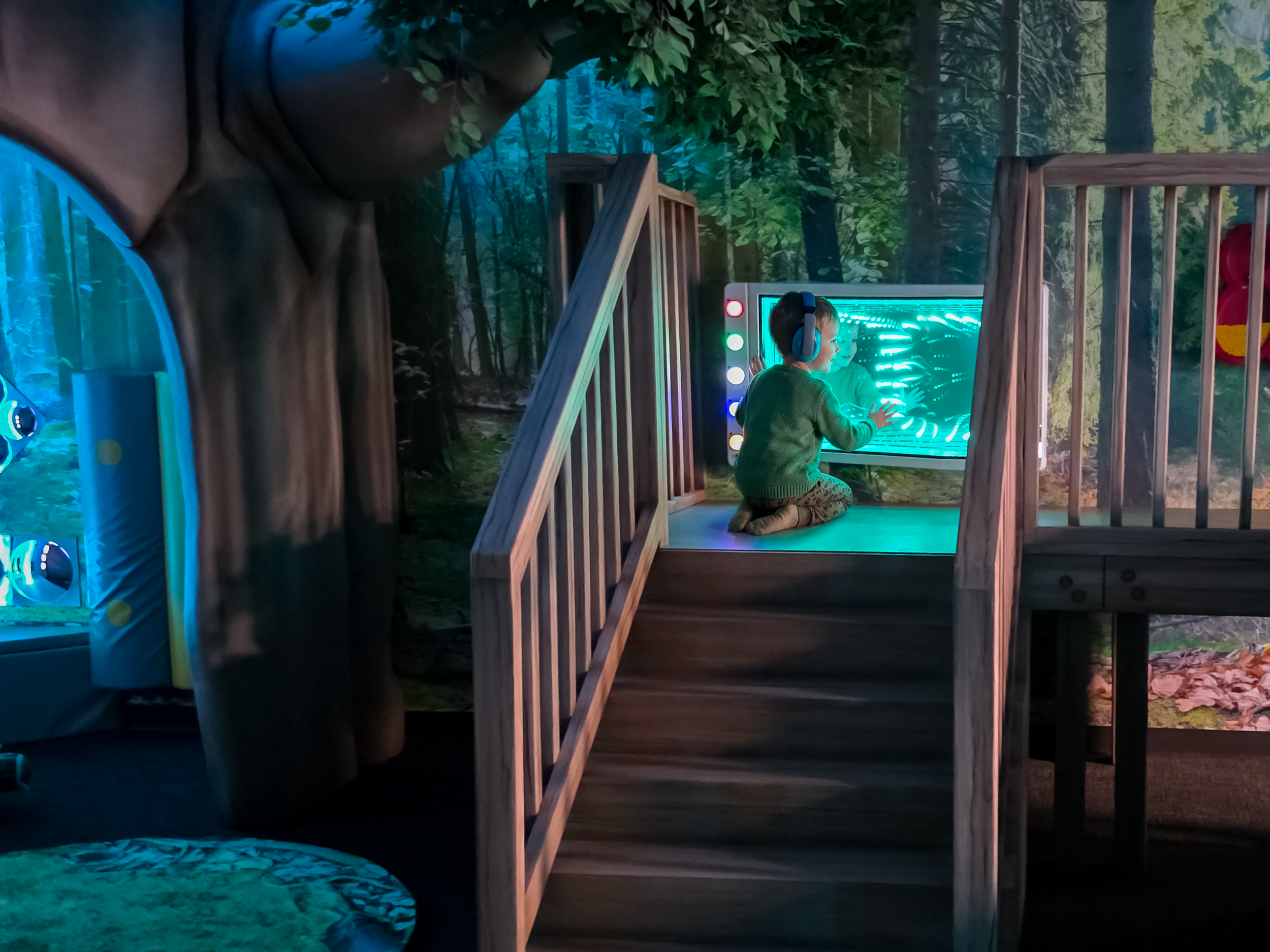 Child explores an illuminated sensory panel on a woodland-themed indoor play structure designed for accessible, hands-on play and discovery.