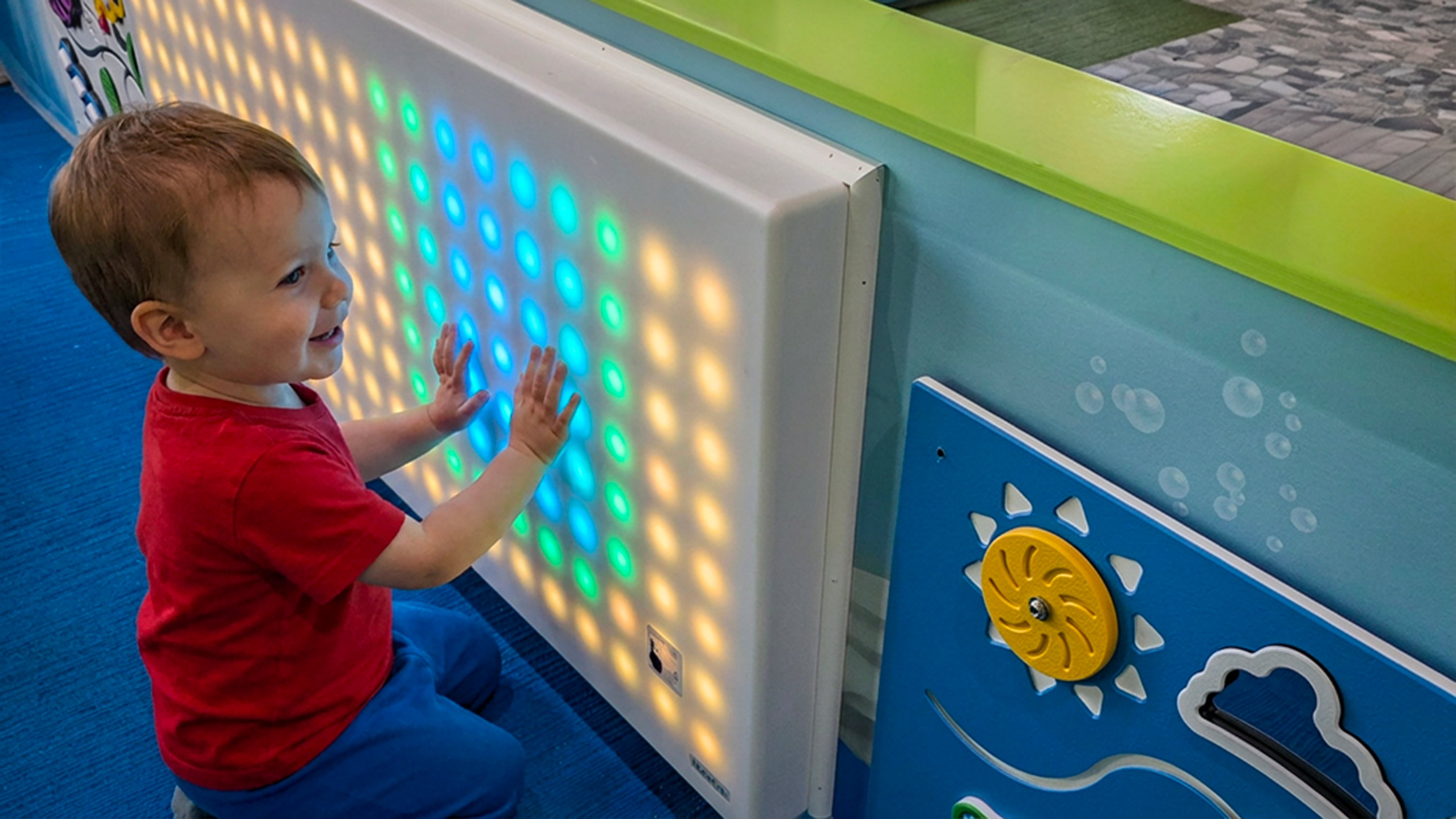 Young child exploring a colorful interactive light panel in a children’s play space, encouraging hands-on discovery and sensory play.