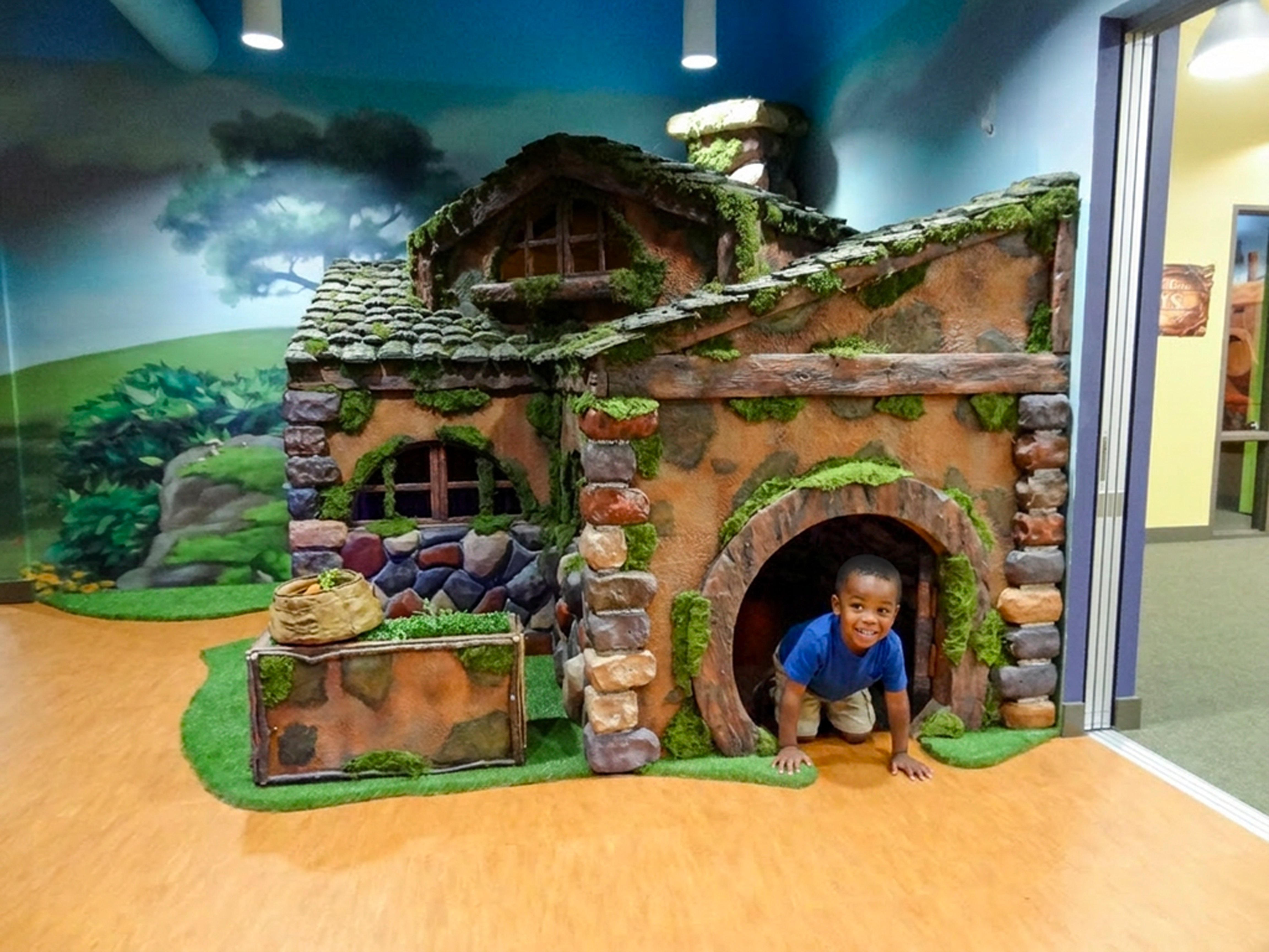 Child crawling through a tunnel in a sculpted storybook cottage designed for imaginative play, exploration and discovery.