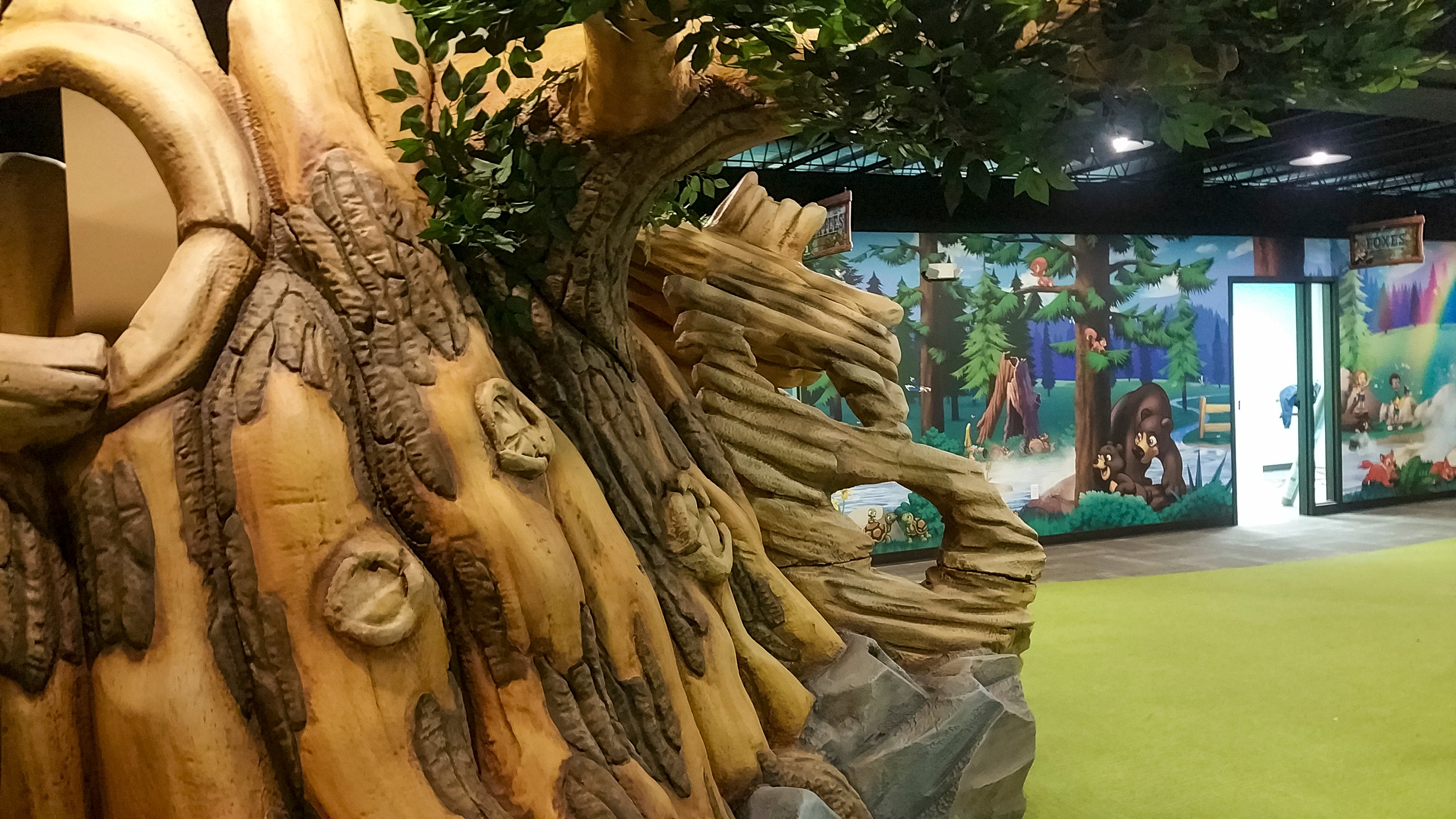 Sculpted tree play feature and custom forest wallcoverings create an immersive camp-themed environment for Faith Community Church's children's ministry.