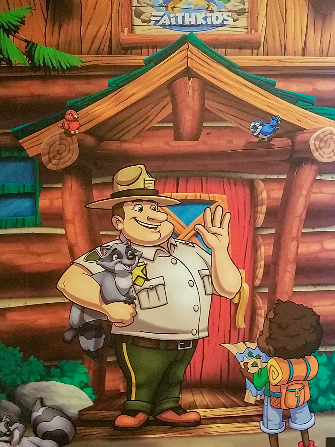 Custom children's ministry mural featuring a friendly park ranger welcoming campers outside the FaithKids lodge at Faith Community Church.