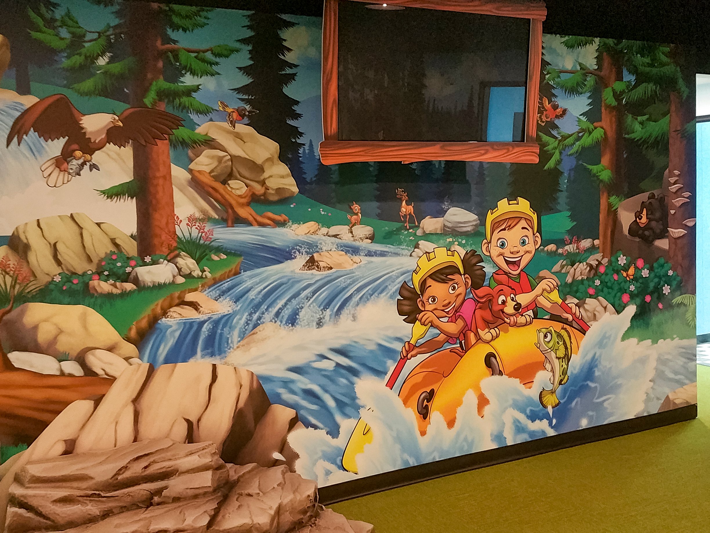 Custom whitewater rafting mural with a themed TV surround extends the camp adventure throughout Faith Community Church's FaithKids children's ministry.