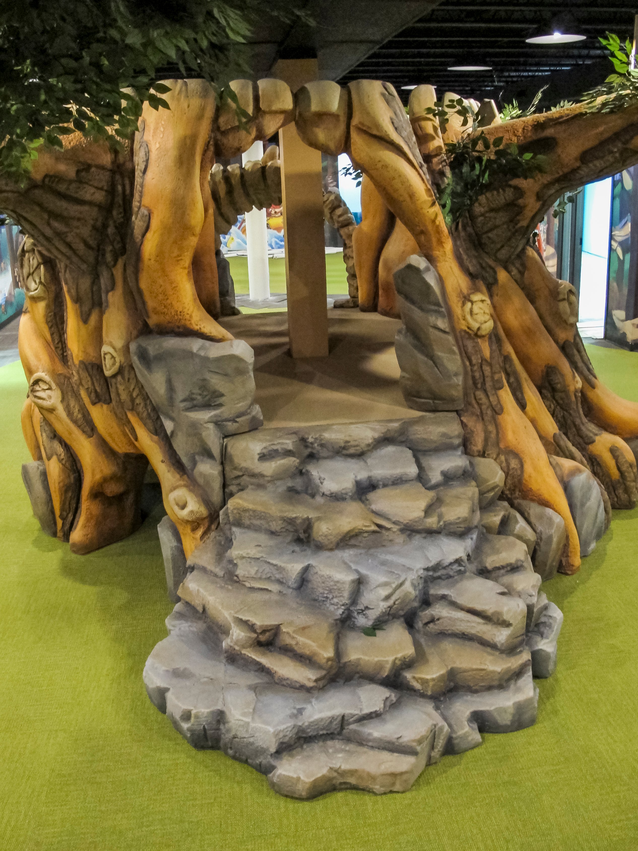 Custom sculpted tree play feature with stone steps leading to an elevated play platform in Faith Community Church's camp-themed children's ministry.