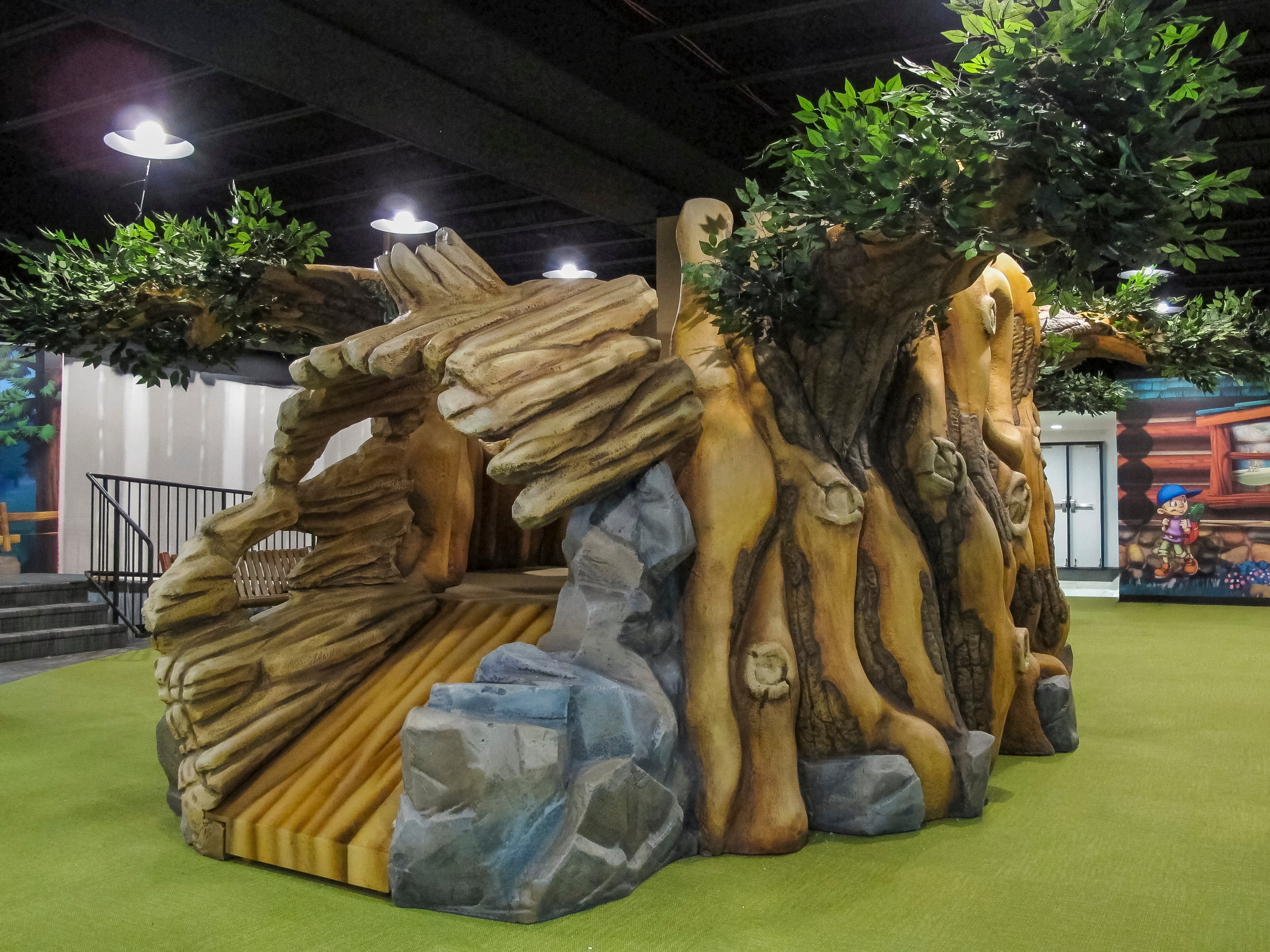 Custom tree play structure with crawl-through tunnel, and climbing features in Faith Community Church's camp-themed children's ministry.