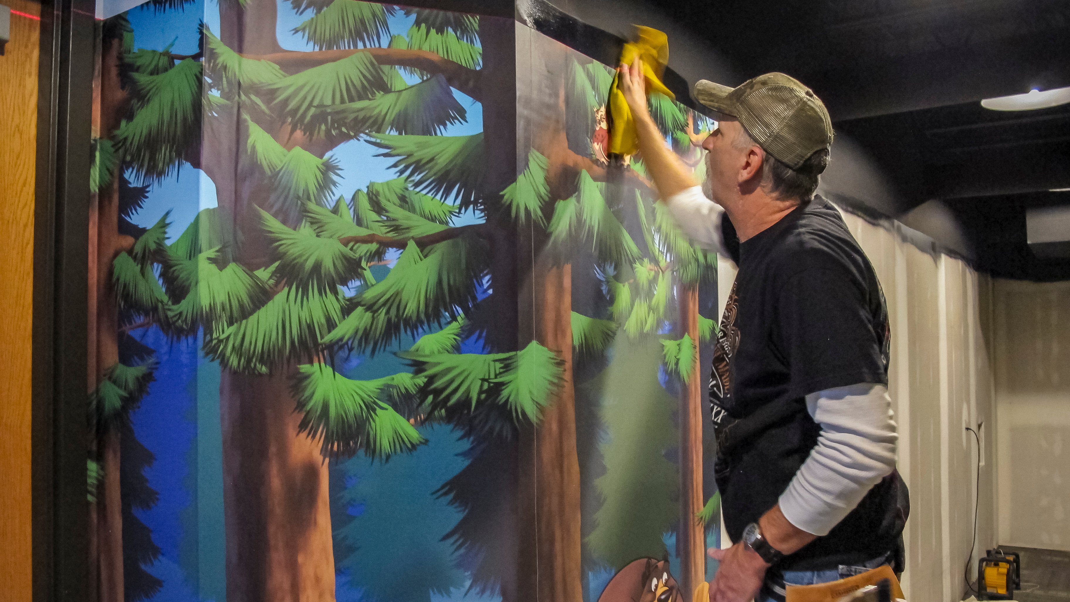 Installer applies custom printed woodland mural wallcoverings in Faith Community Church's camp-themed FaithKids children's ministry.