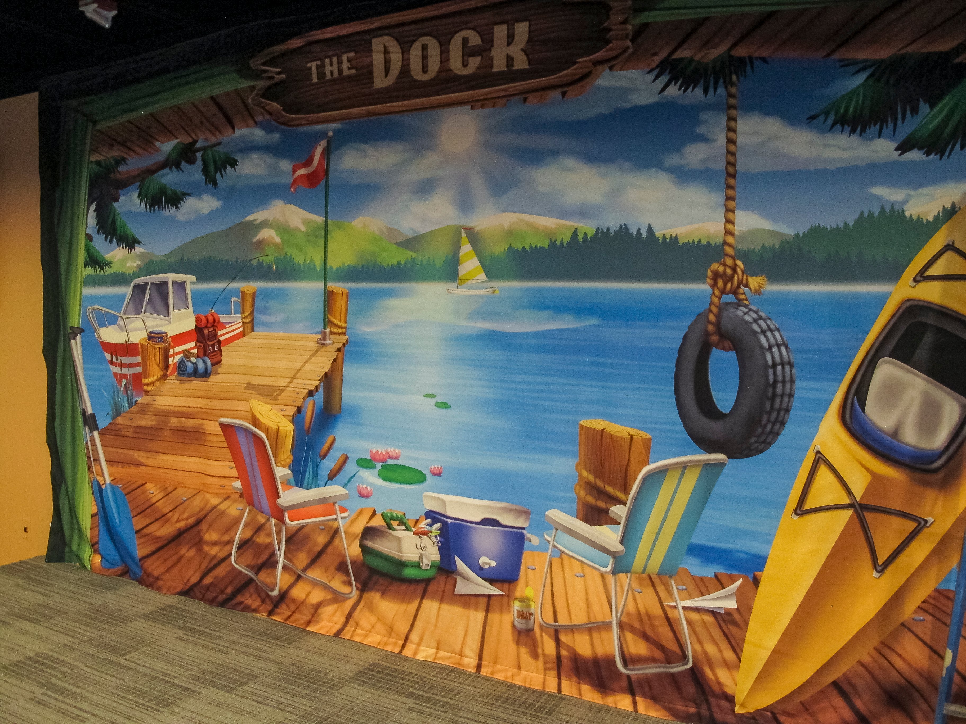 Custom lakeside dock mural featuring boating, fishing, and camping imagery in Faith Community Church's camp-themed children's ministry.
