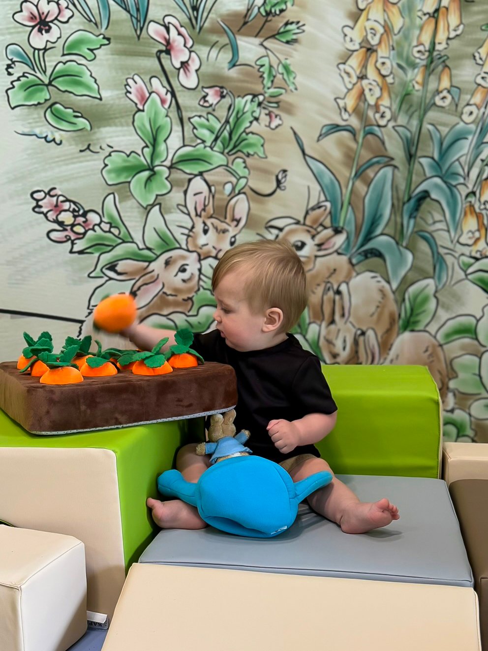 Young child explores an interactive garden feature in front of a nature-themed mural, supporting sensory play and discovery.