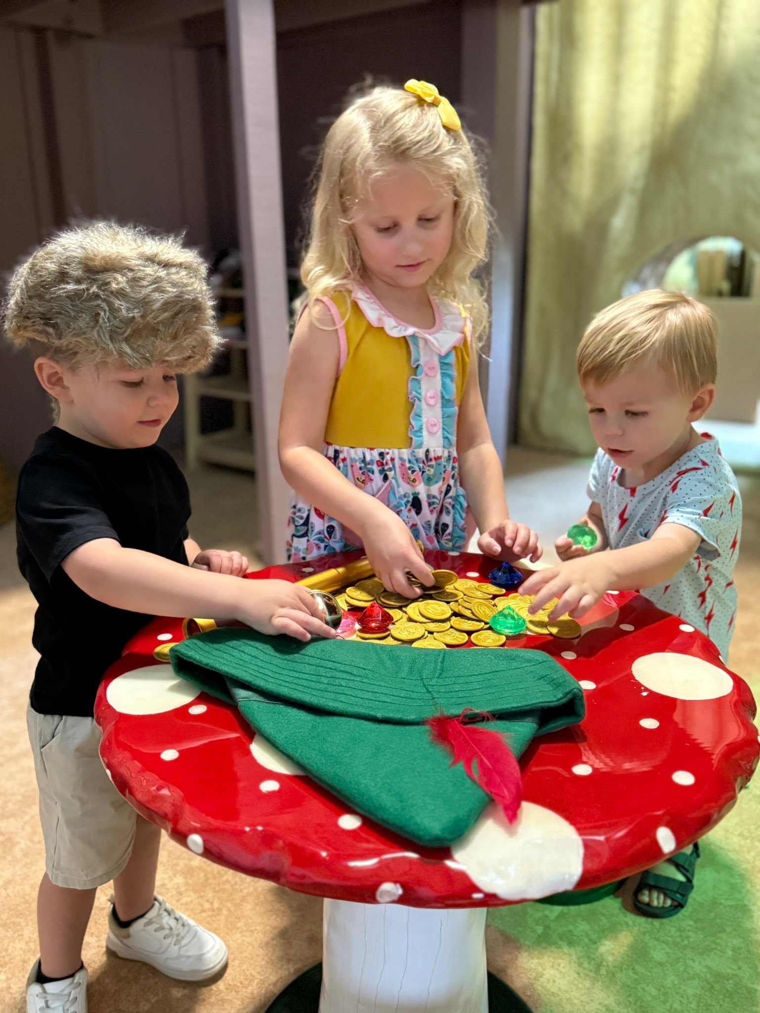 Three children engage together at a colorful mushroom-shaped sensory play table, encouraging hands-on exploration and social play.