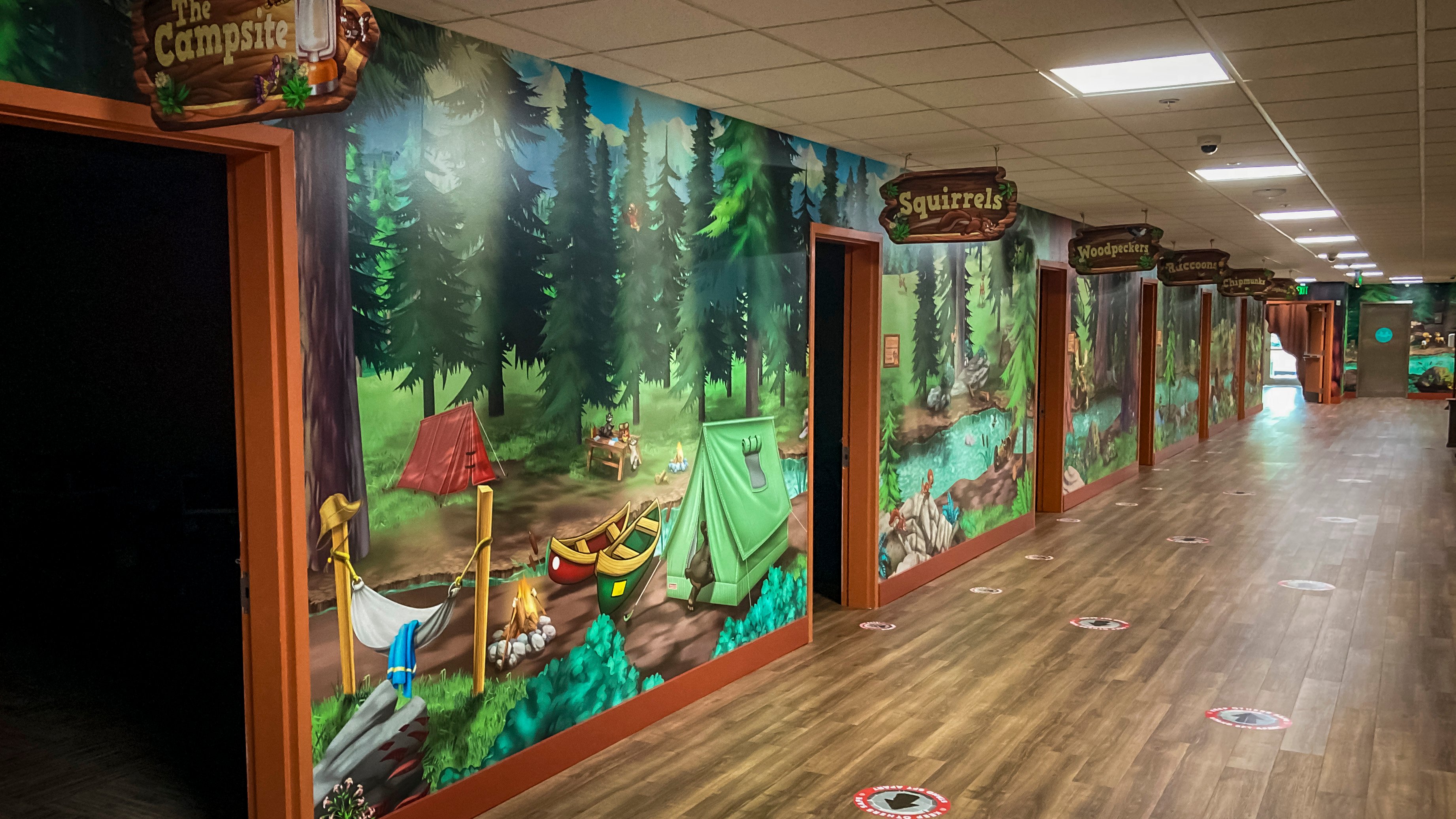 Forest-themed children’s hallway with colorful camping murals, animal room signs and visual details that encourage exploration and discovery.