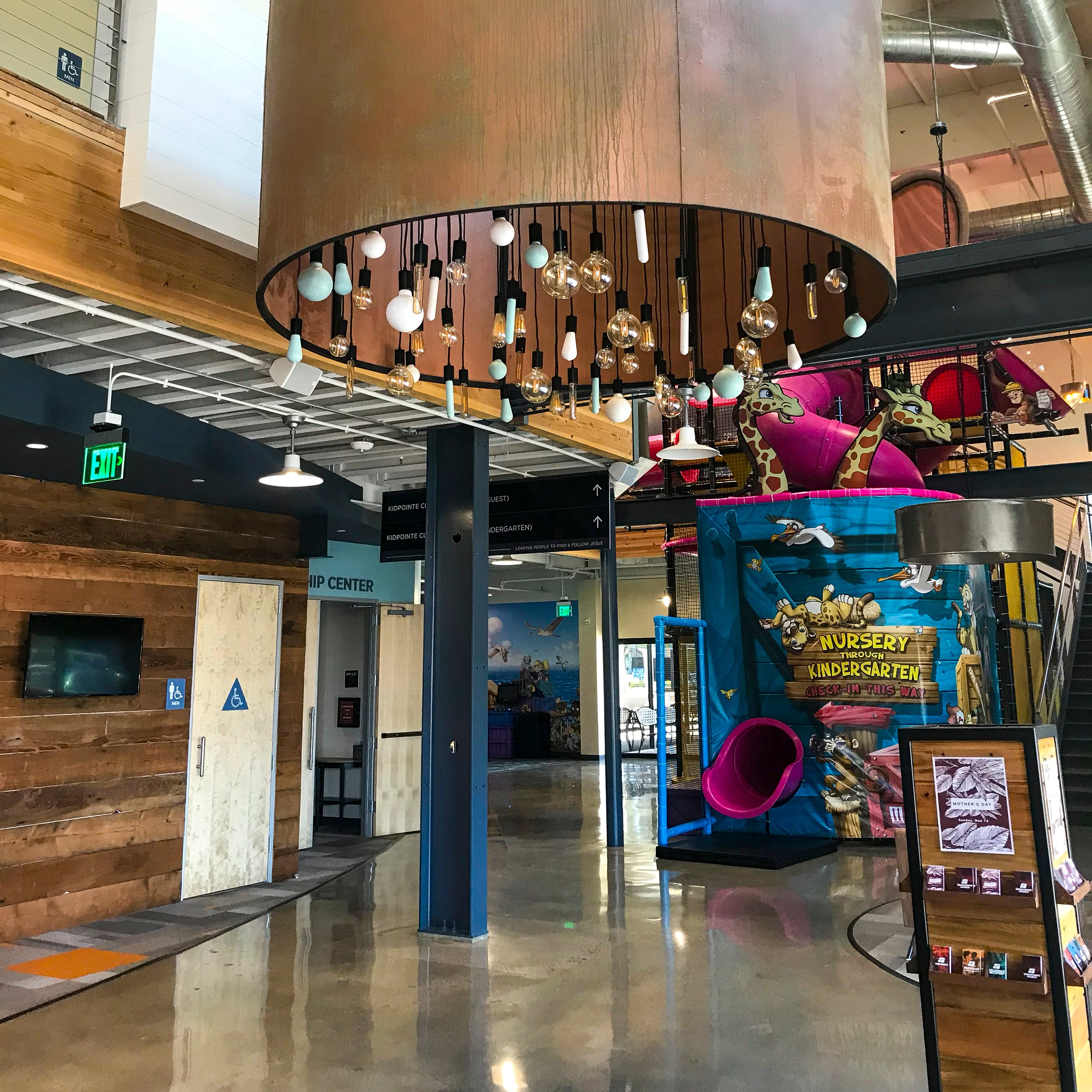 Modern church lobby with neutral finishes and a colorful children's ministry play area creating a clear family-friendly destination.