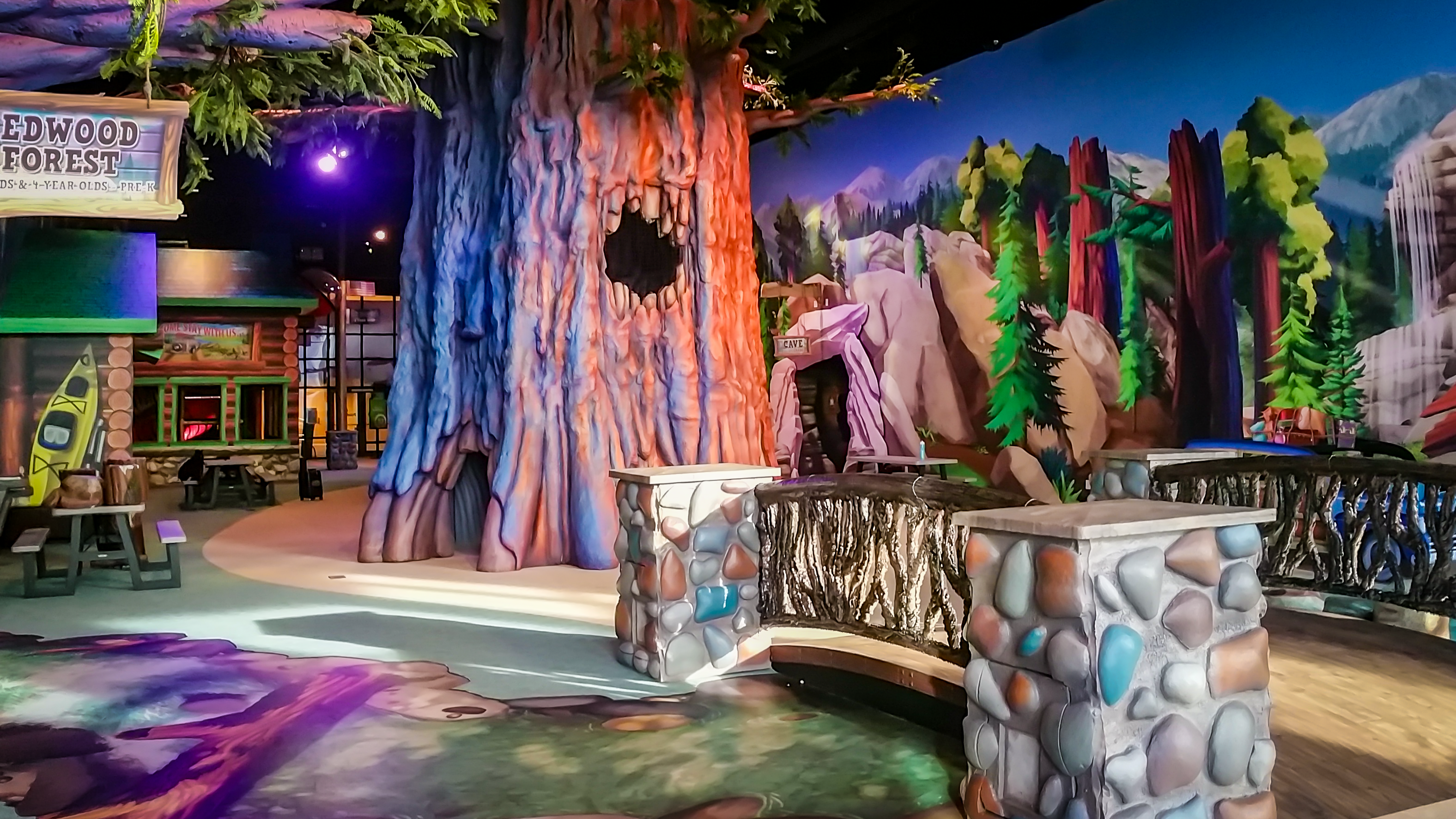 Immersive forest-themed indoor play environment with a giant tree, rockwork, bridge and colorful nature murals designed for exploration.