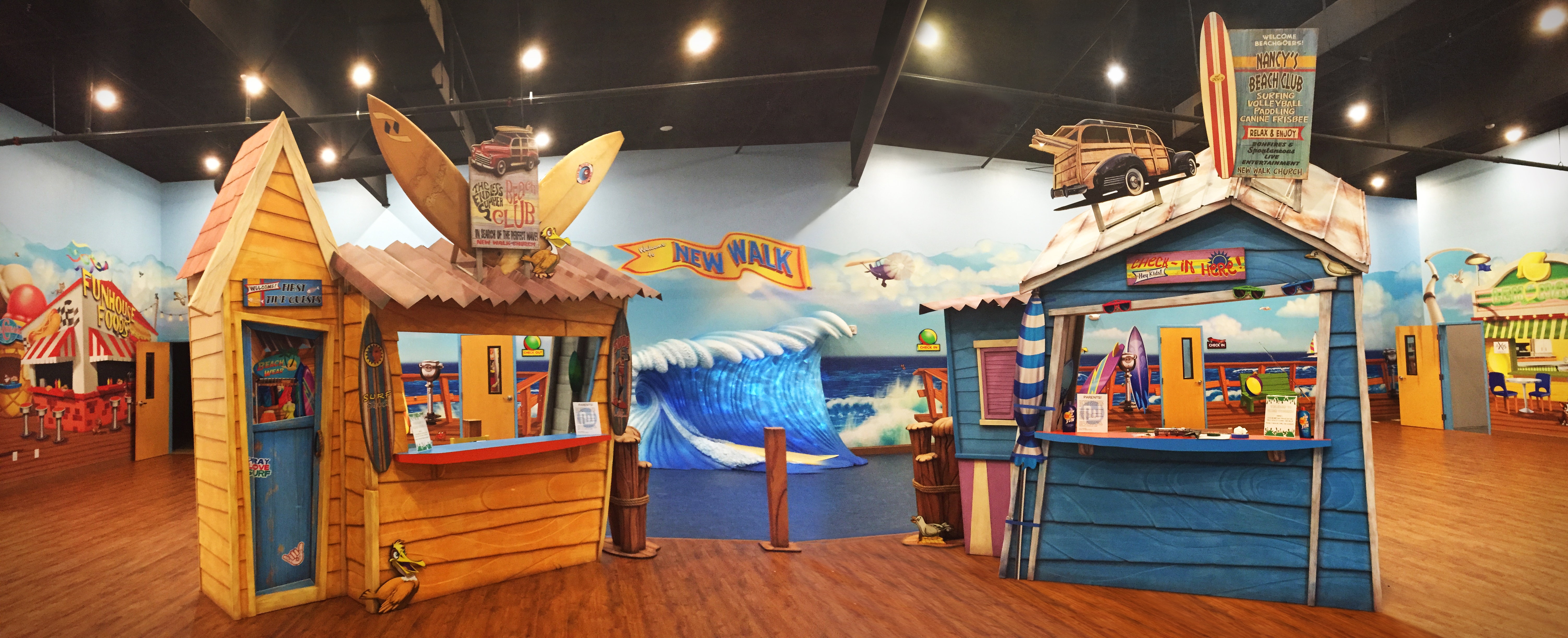 Beach-themed children's ministry check-in area at New Walk Church, featuring colorful surf shack counters, surfboards, and ocean murals that create a welcoming arrival experience for families.