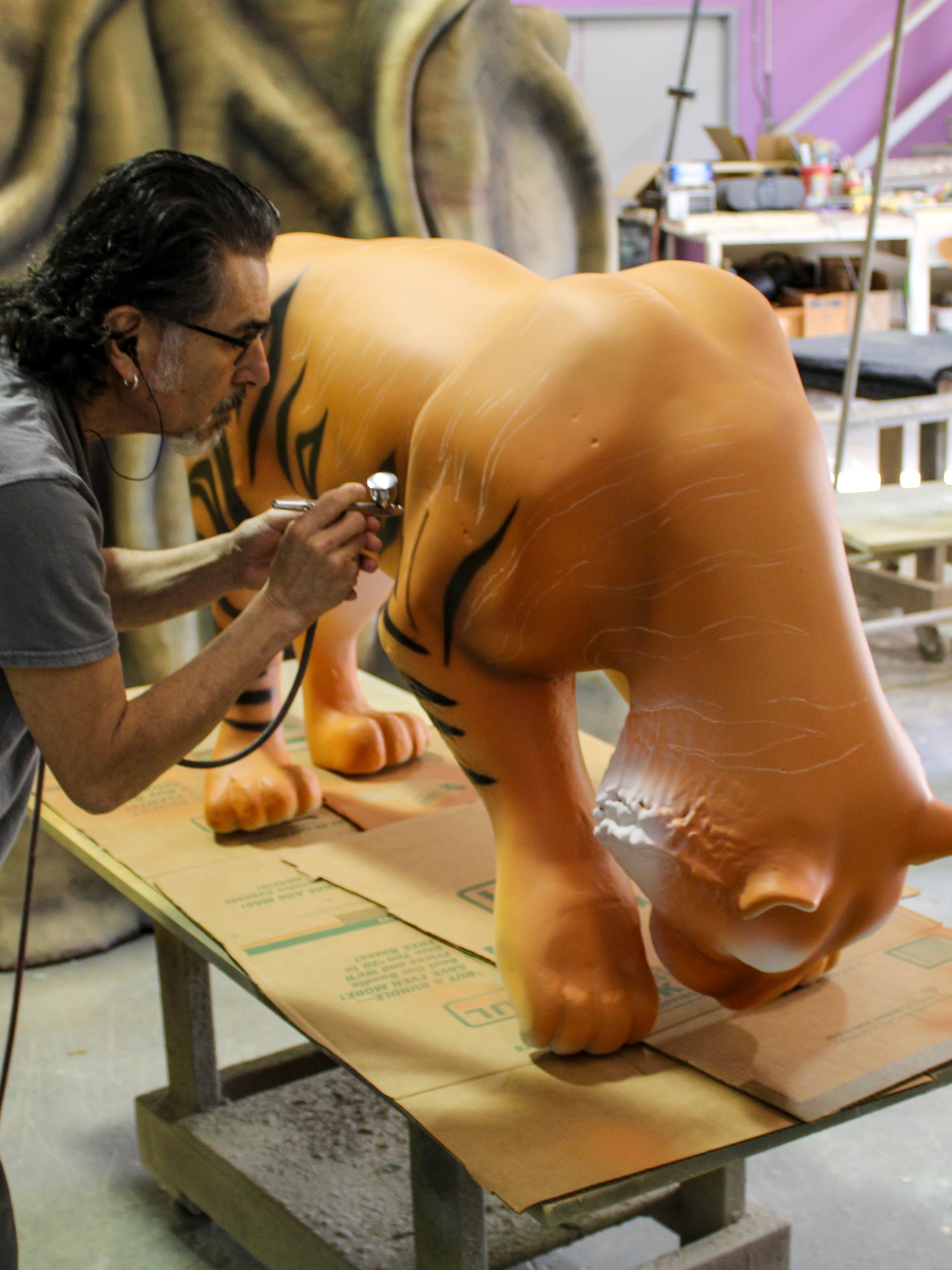 Artist hand-paints a custom tiger sculpture in the fabrication shop, adding realistic details to a themed environment feature.
