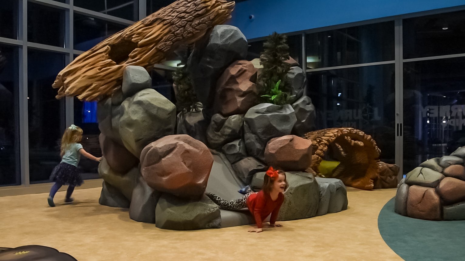 Children climb, crawl, and explore a custom rock-themed play structure designed to encourage active play and discovery.