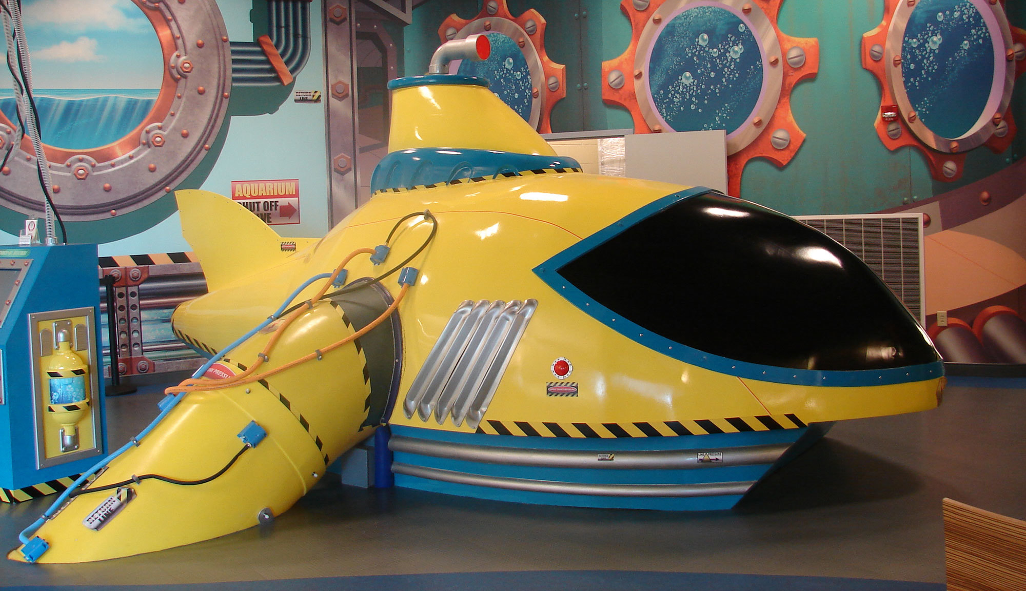 3D Sculpted Yellow Submarine in Undersea Themed Space with porthole murals behind it.