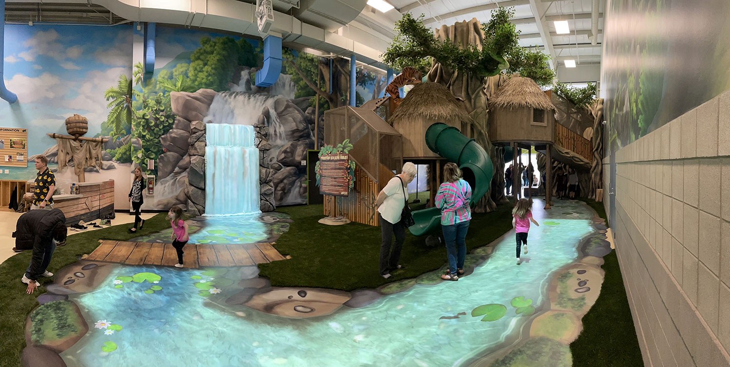 West Chicago Park District Treetop Escape themed environment featuring an animated river and waterfall, 3D Sculpted giant tree with treehouse and slides.