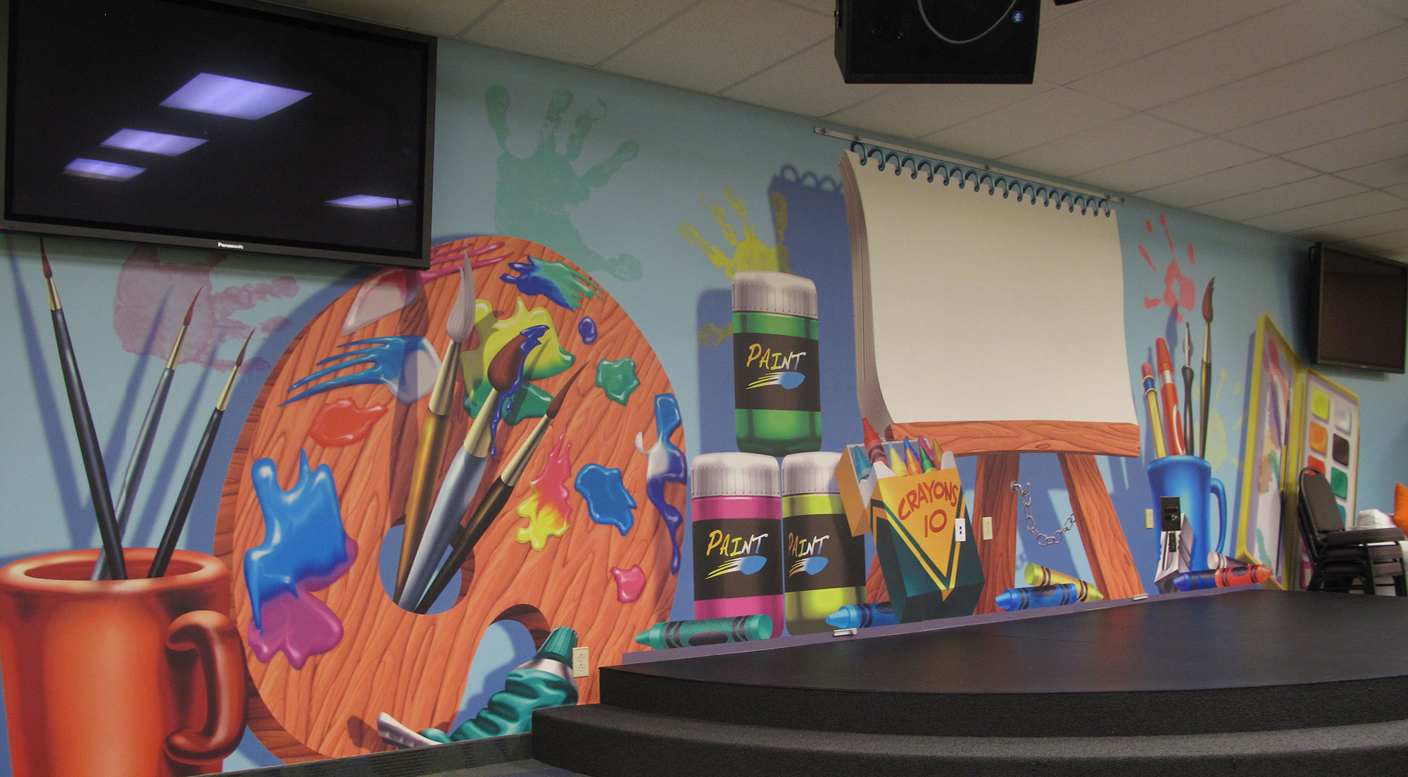 Art Class Themed Environment backdrop for stage at Bent Tree Bible Fellowship with large Easel, Paint Palette, Cup of brushes, Crayons and more.