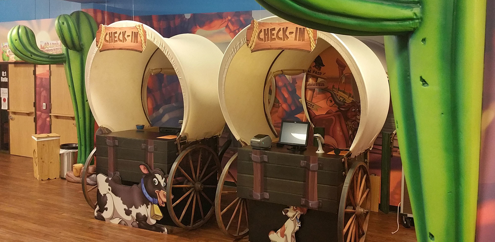 2 life-sized Covered Wagons with sculpted cacti as check in stations in a Western Themed space at Crossroads church in Odessa TX