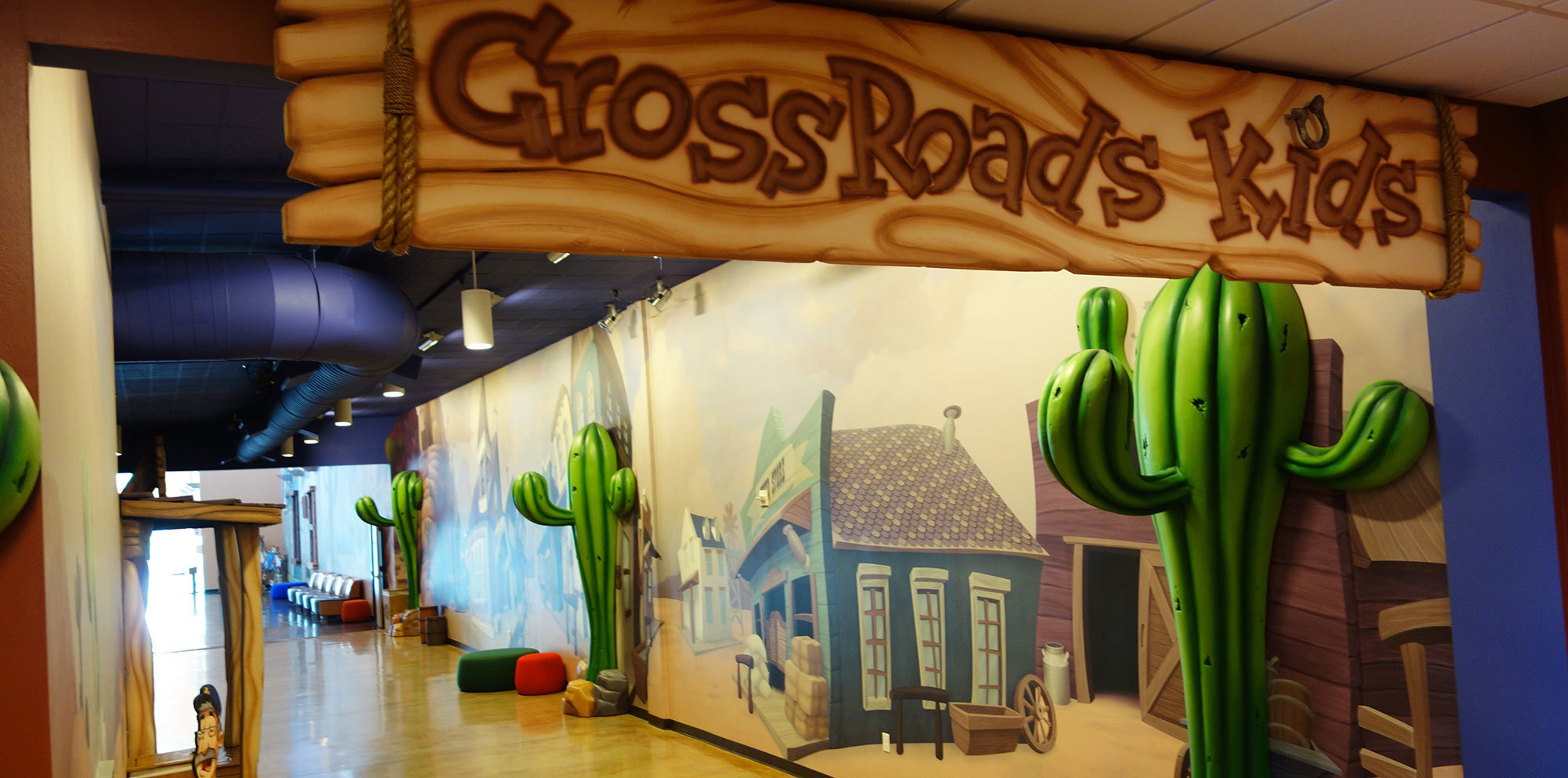 Western Themed Space with 3D cacti, wall murals of old west buildings and a sign reading "Crossroad's Kids" in a faux wood style at Crossroads Church TX