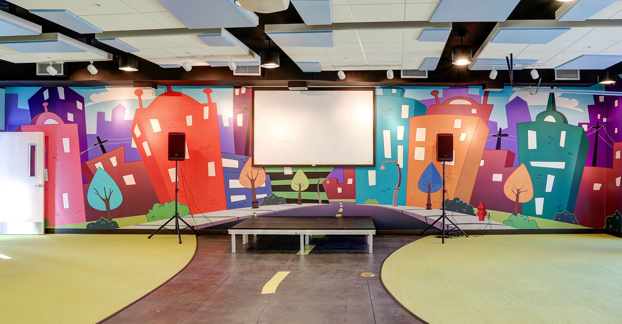 Stylized city themed Stage with colorful wacky buildings, and a white projection screen at Mount of Olives