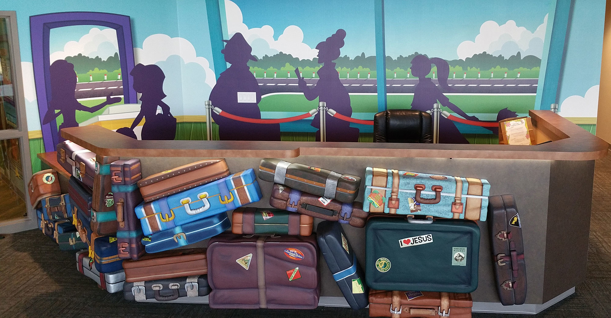 Airport Themed Check-in desk with 3D relief luggage stacked in front of the counter and a large wall mural of an airport scene behind it.