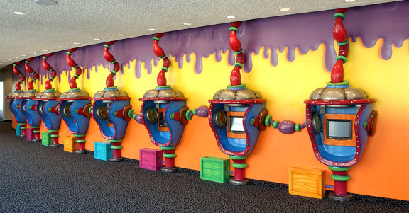 8 Wacky Slime Factory styled 3D Check-in Kiosks and Gaming Stations along a wall painted yellow, orange and purple.