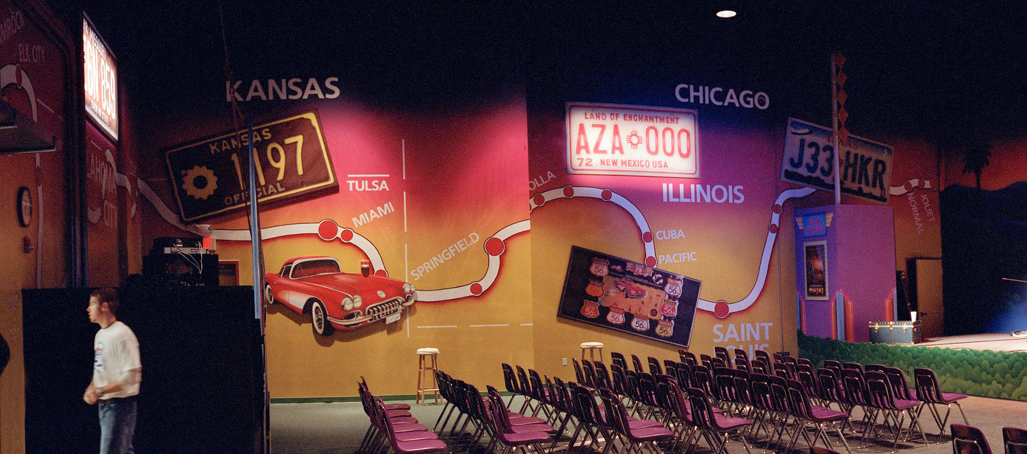 Travel License Plate Themed Sound Panels on a wall mural of a map with city names and a red 50s corvette car in a Church Auditorium