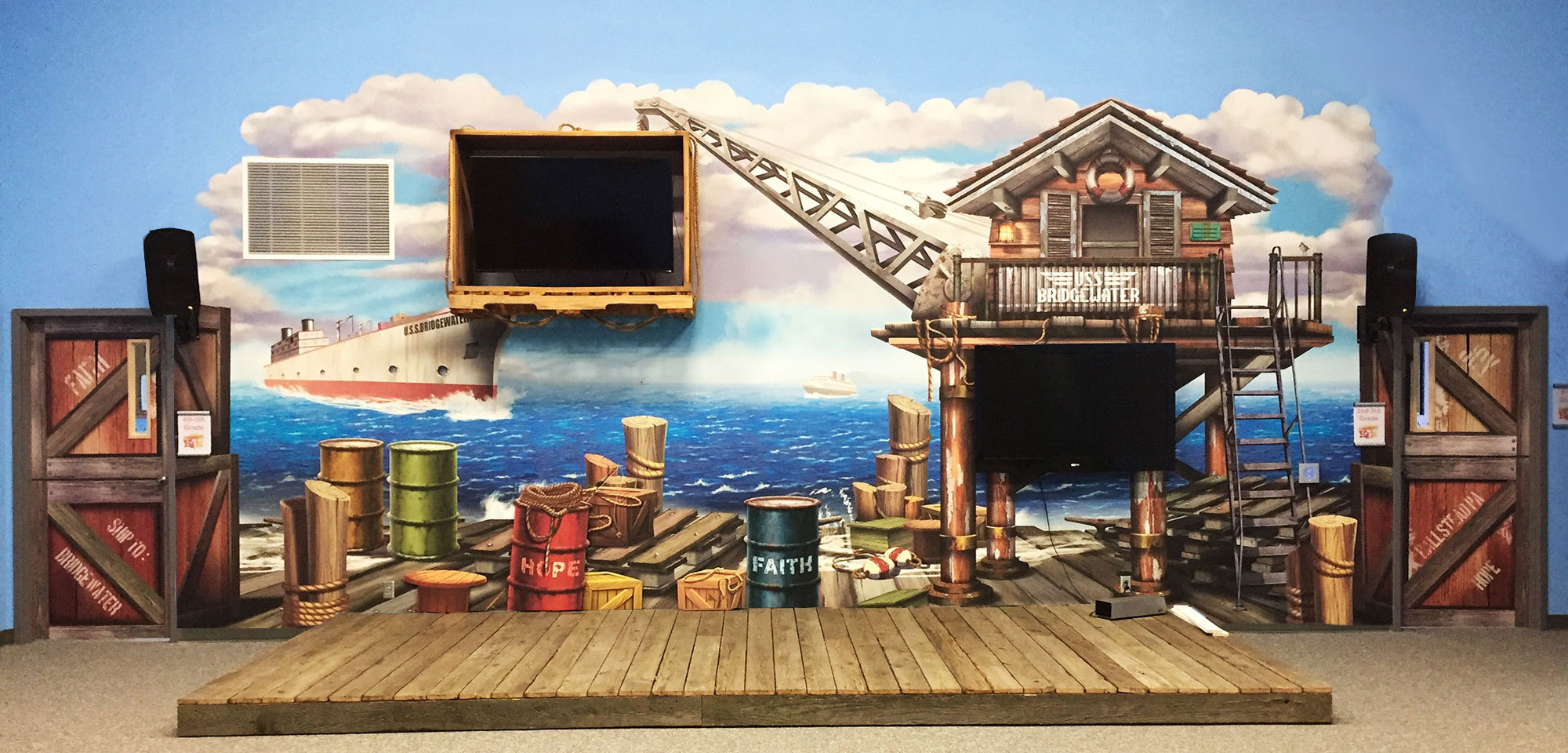 Shipping Dock Themed wall mural with crates, barrels and crane shed holding a wooden 3D TV surround on a wooden stage