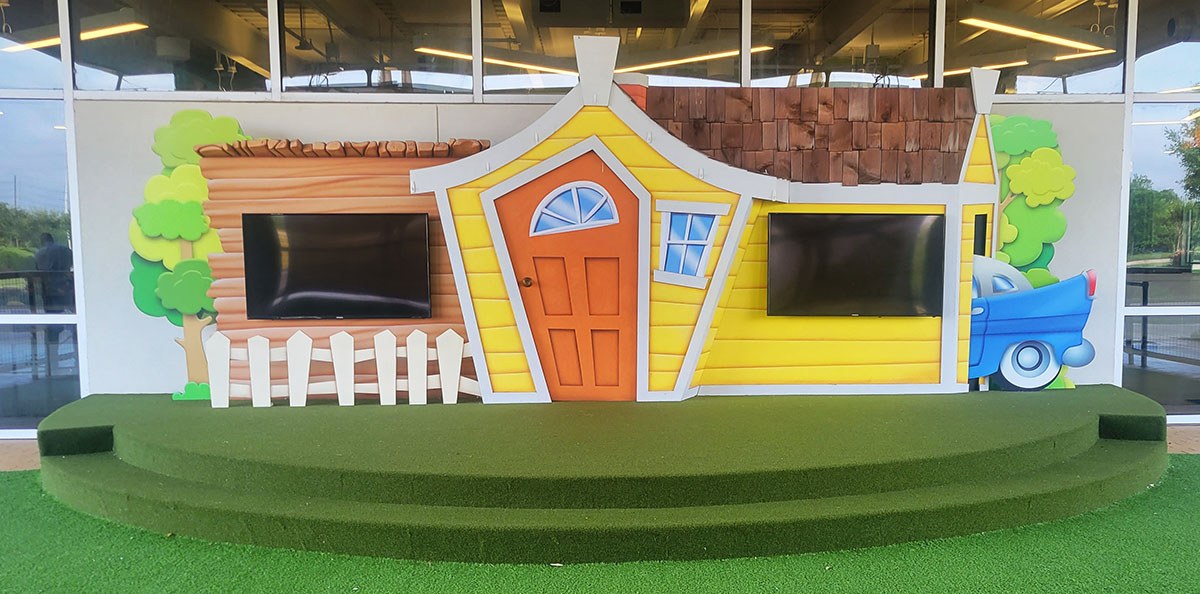Stage backdrop with Yellow house, blue car, orange door and green astro turf ground cover