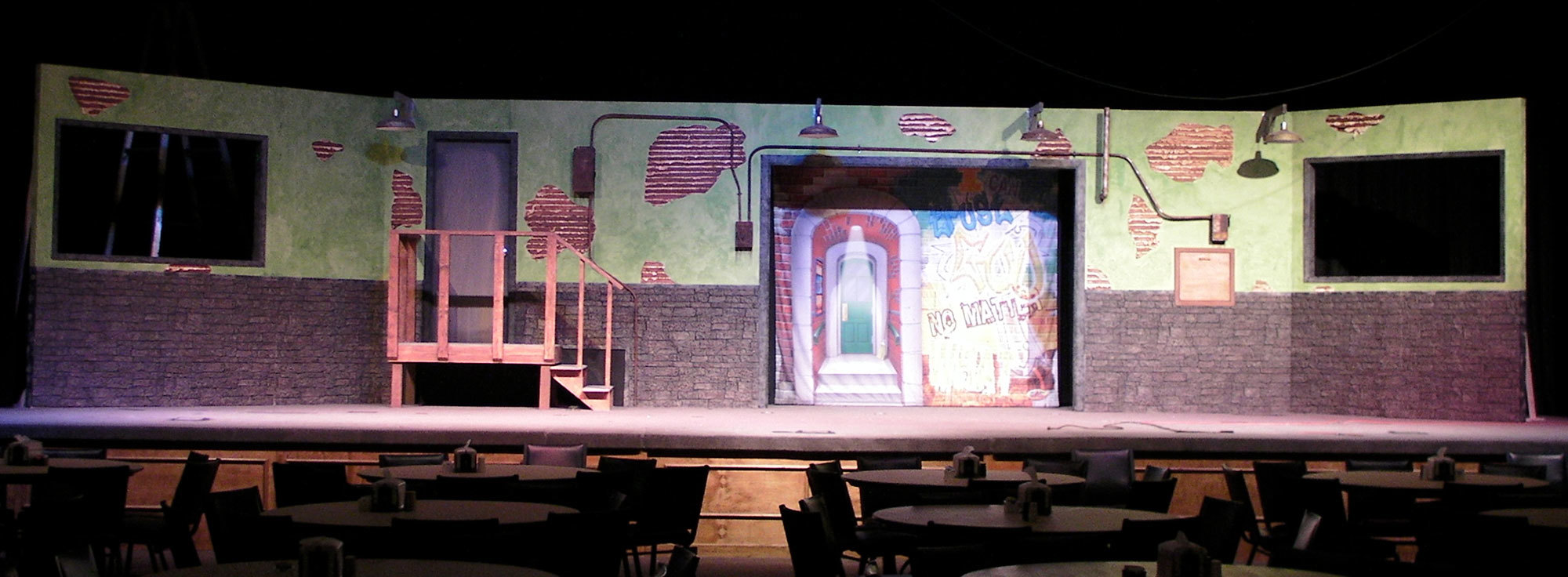 Big City Themed Stage Set with distressed old brick walls, a wooden staircase and two TV displays.