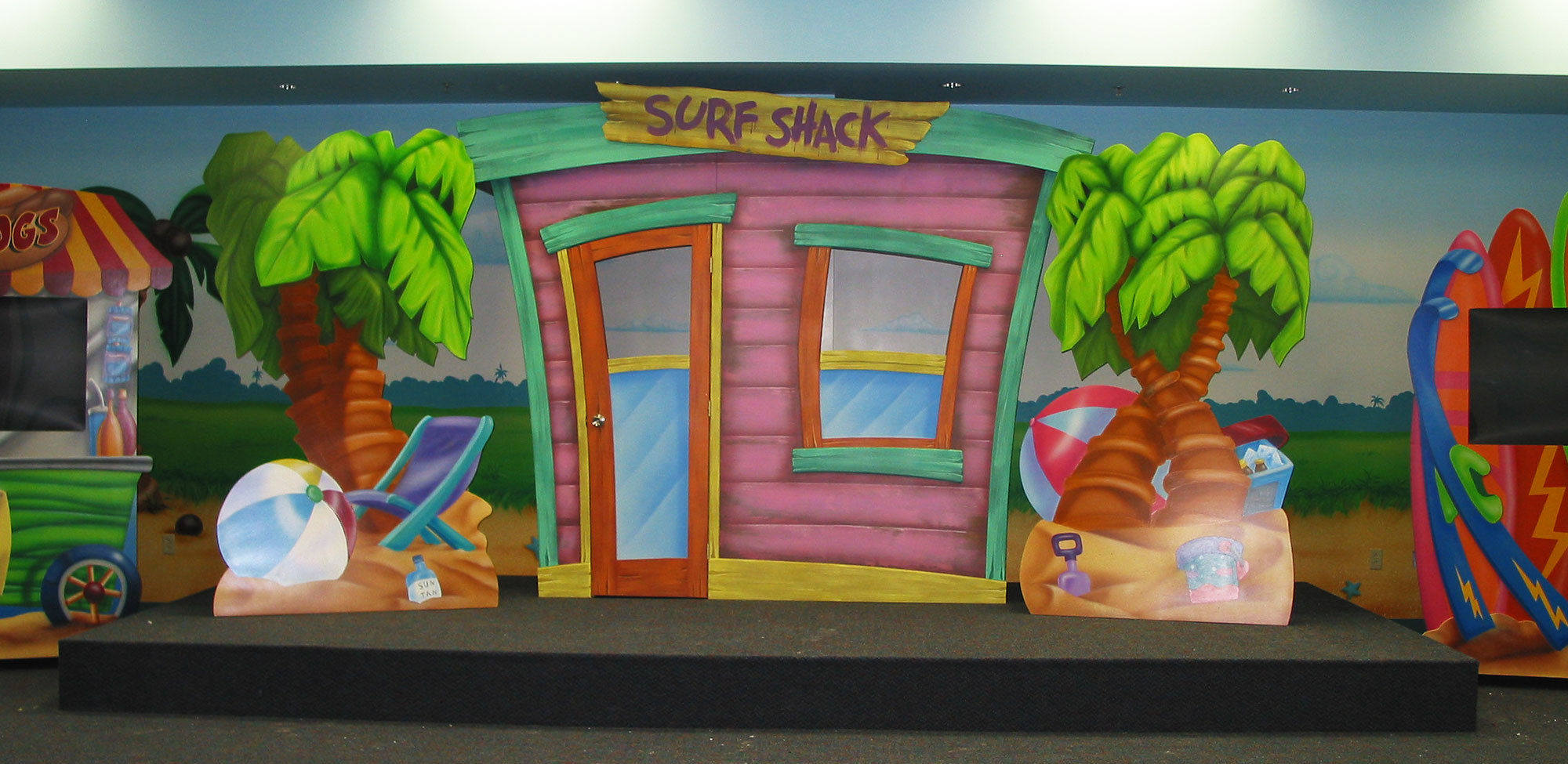 Beach Themed Stage with 2D Surf shack, palm trees, beach balls and chairs.