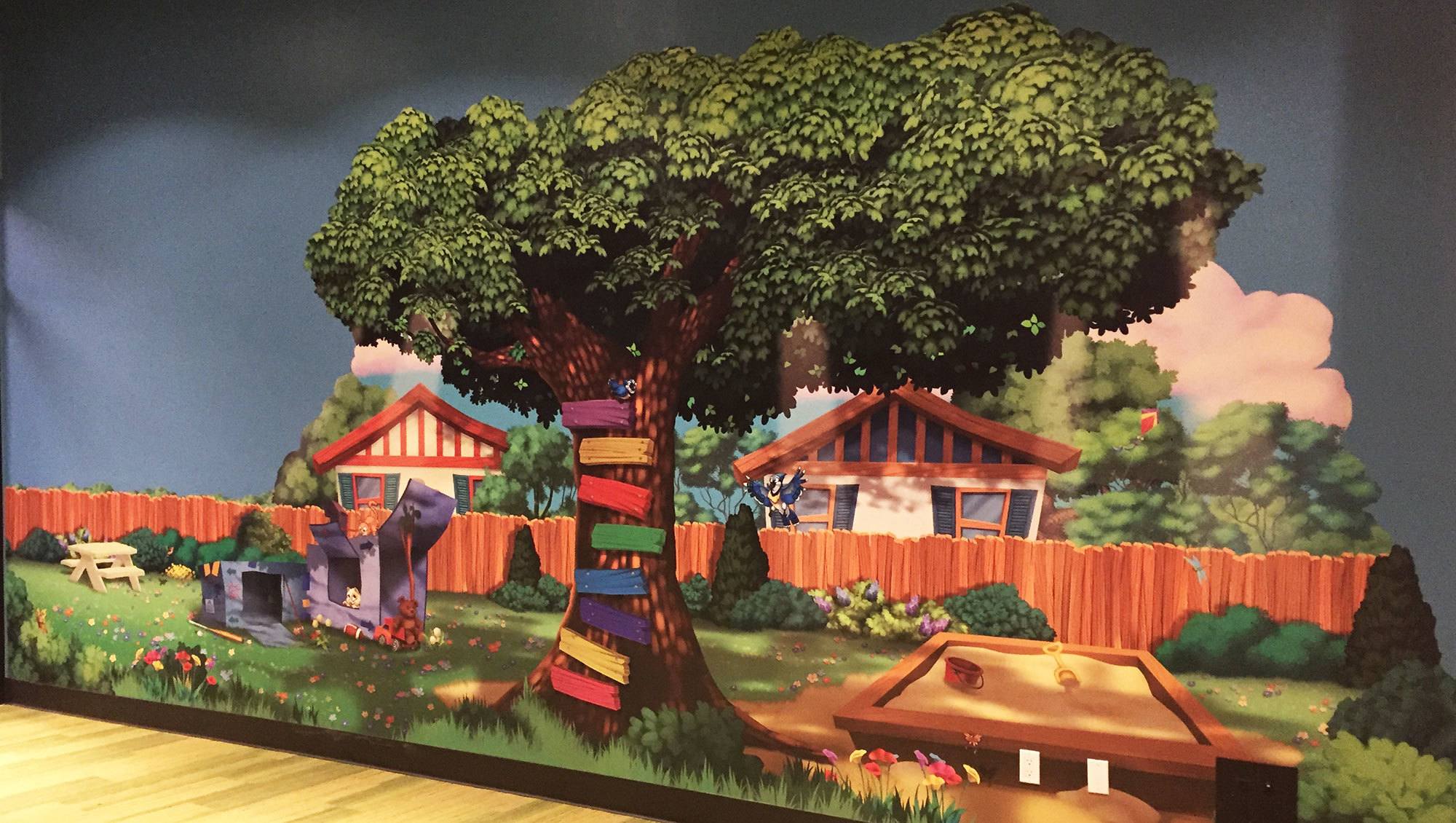 Neighborhood Themed Wall Covering with large tree, cardboard clubhouse, sandbox, wooden fence and 2 houses at Christ Fellowship Church