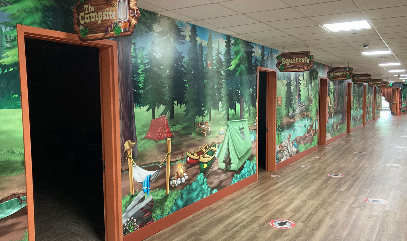 Camping Themed hallway with full wall murals of forest scene and 2D cutout classroom signage.