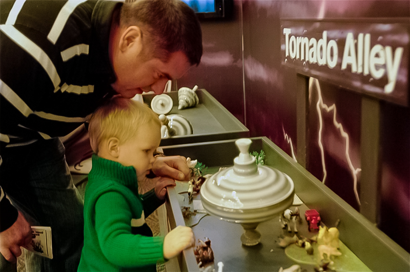 Father and young child exploring an interactive tornado exhibit together in a themed children's play space, encouraging hands-on learning and shared discovery.