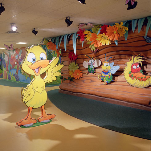 Cutout of 2D Duck standing in hallway in front of Bugs & Butterflies themed wall covering and cutouts of bugs.