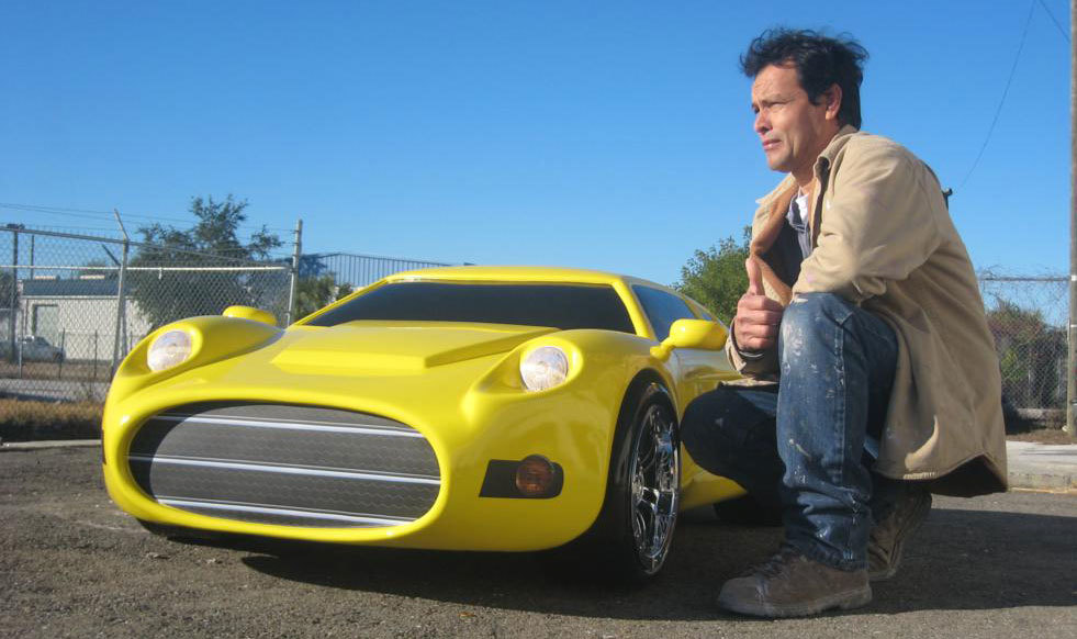 A man squatting next to a Tiny yellow 3D Sculpted Sports Car
