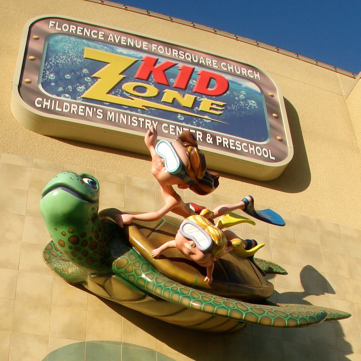 3D relief Sculpted Sea Turtle with two snorkeling kids riding on its back plus a sign for Florence Avenue Foursquare Church Kid Zone mounted high on an outside wall of a building.