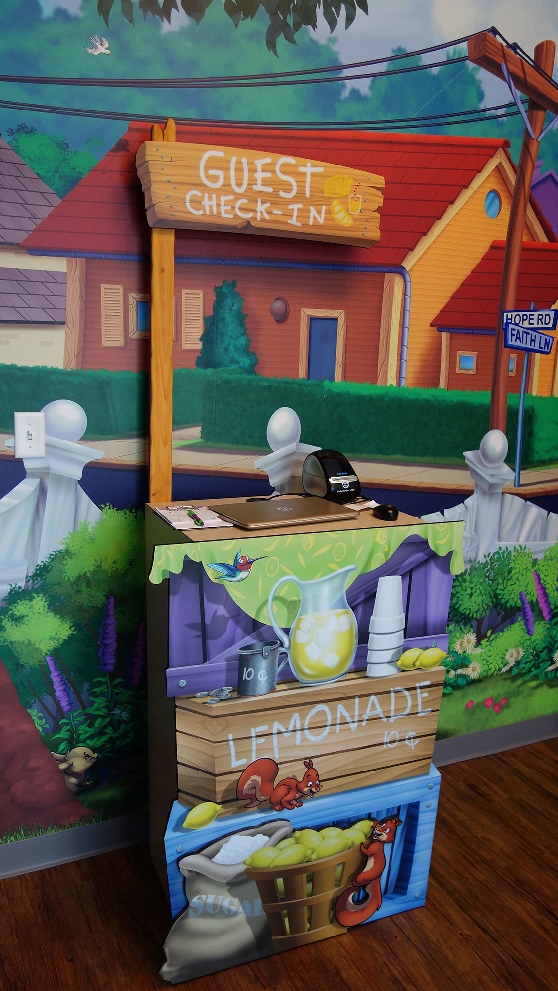 Neighborhood mural scene behind a 2D cutout Lemonade stand as a check-in kiosk at Avalon Church