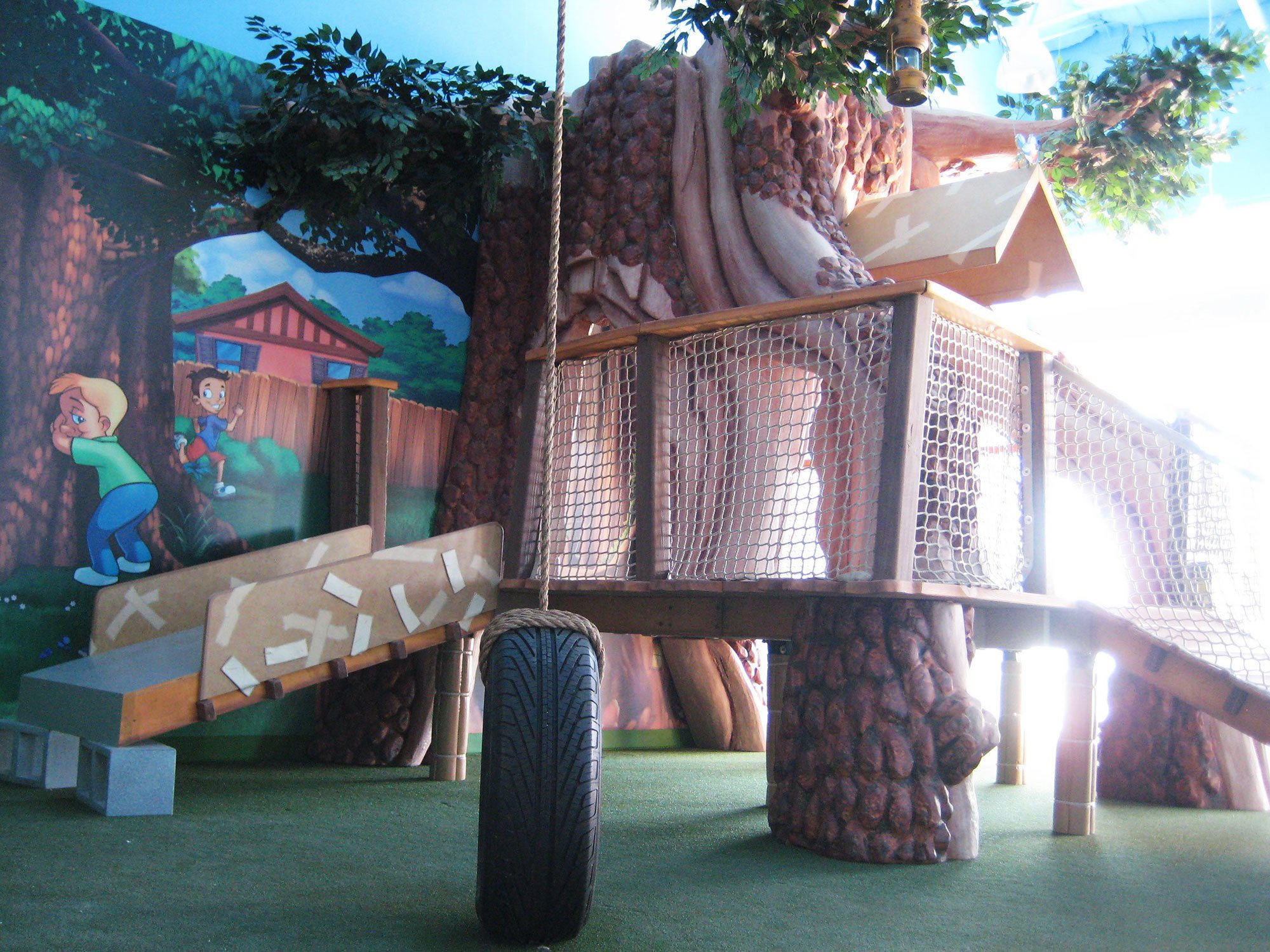 Large 3D sculpted Tree with netted sides and a 3D tire swing in a Treehouse and Neighborhood Themed Environment at Ashley's Playhouse