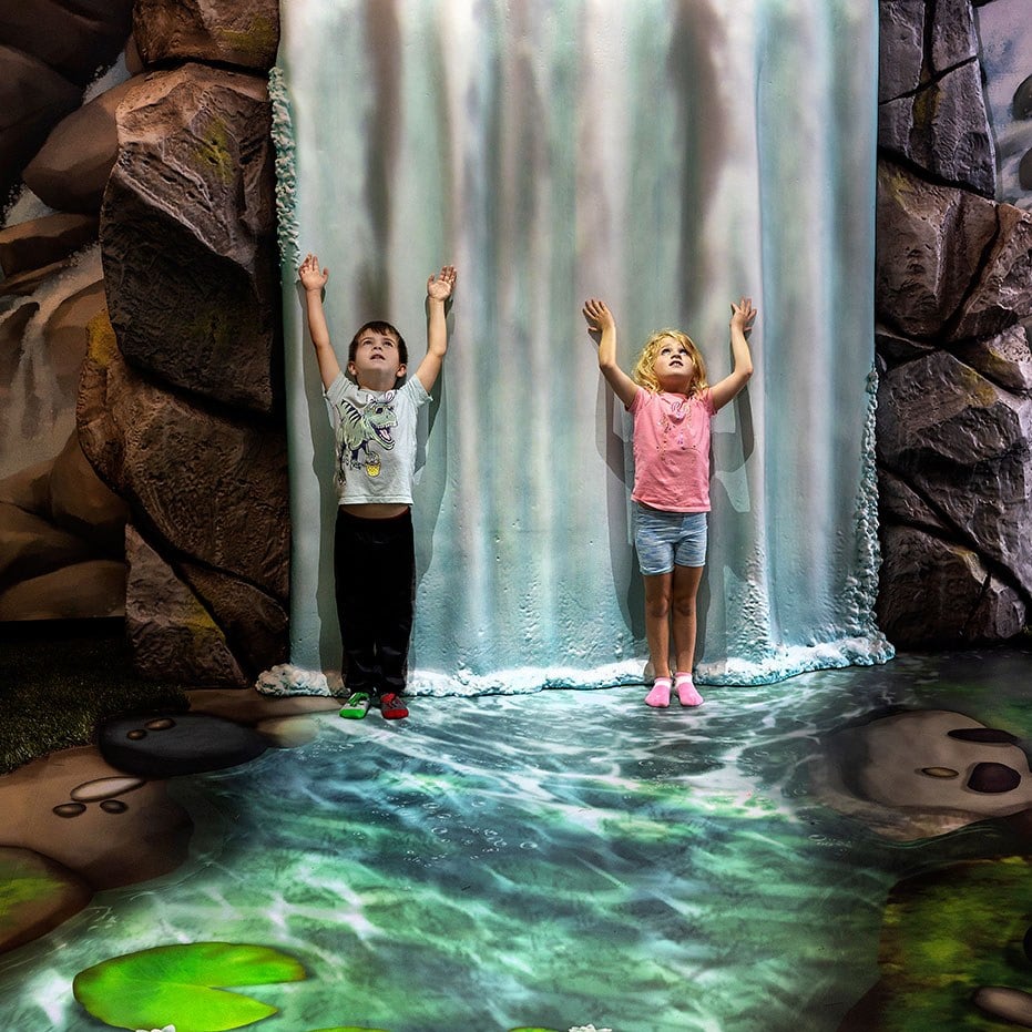 2 kids standing in front of Giant Waterfall animation feature at West Chicago Parks District ARC Center