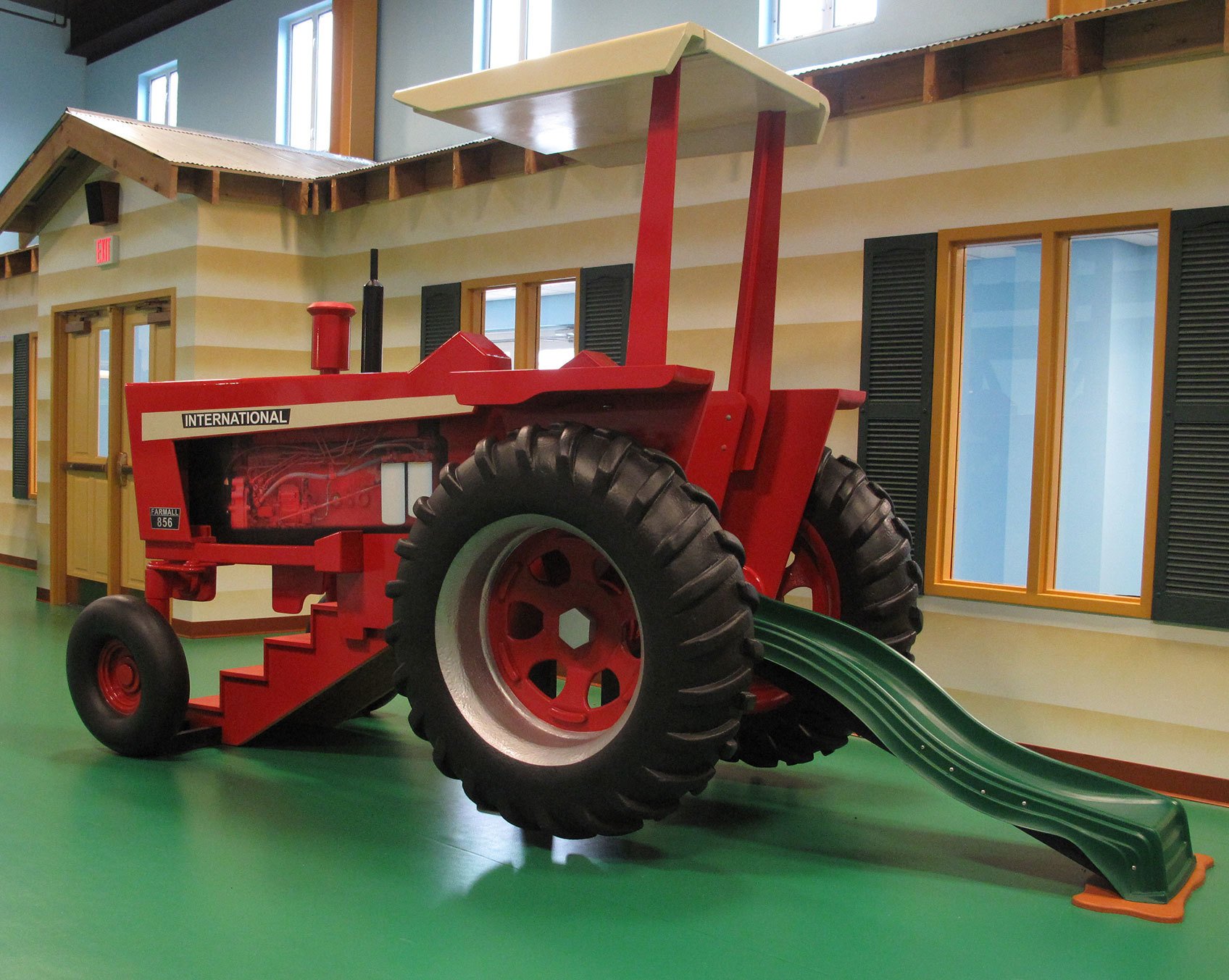 Life sized 3D Red Tractor with stairs and green slide in front of Yellow barn facade in a Farm Themed Space at Hardin Baptist Church