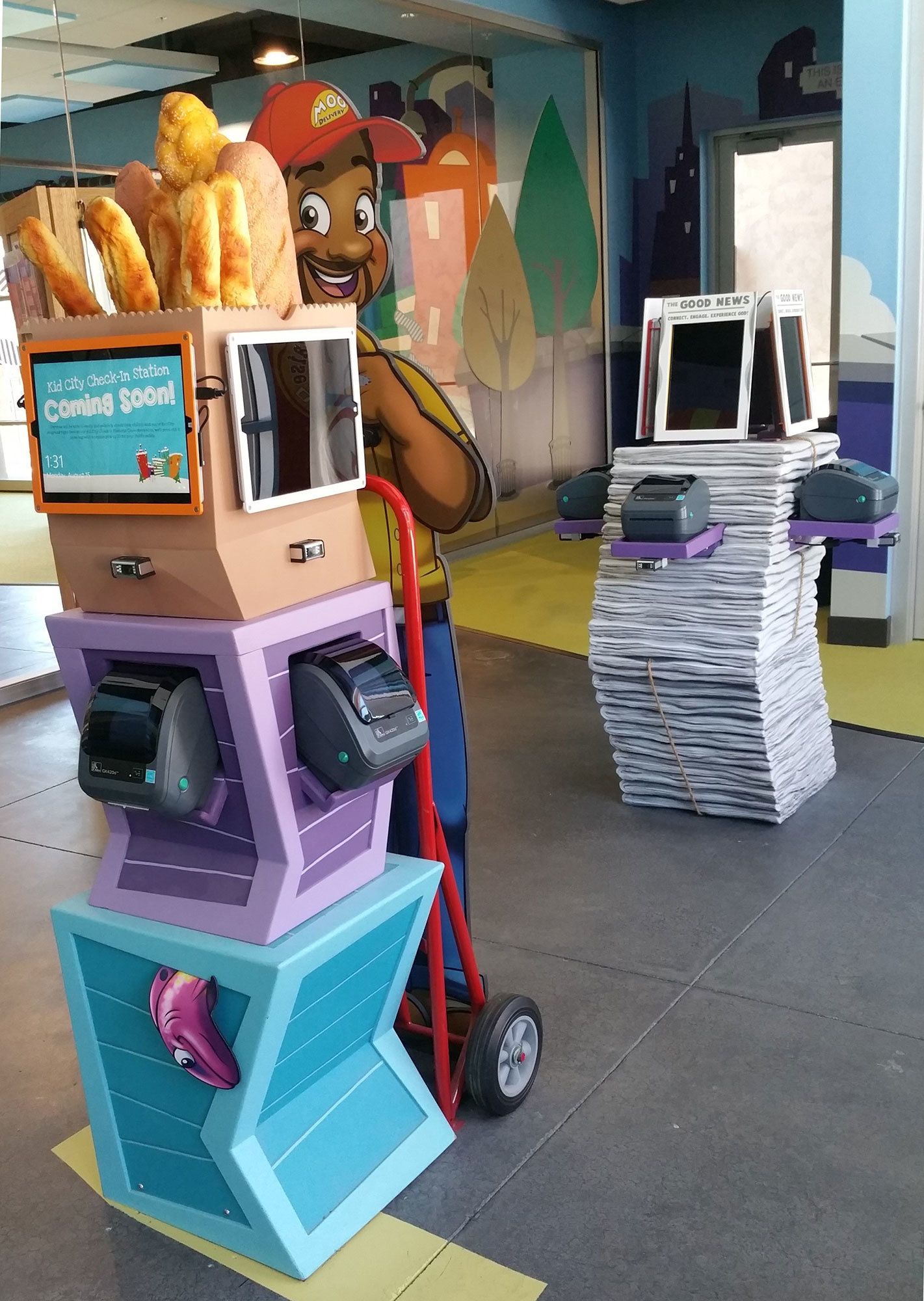 2D cut-out Delivery Man and 3D stacked crates 3-station Check-In Kiosk in Big City Toon Town Themed Space at Mount of Olives Church