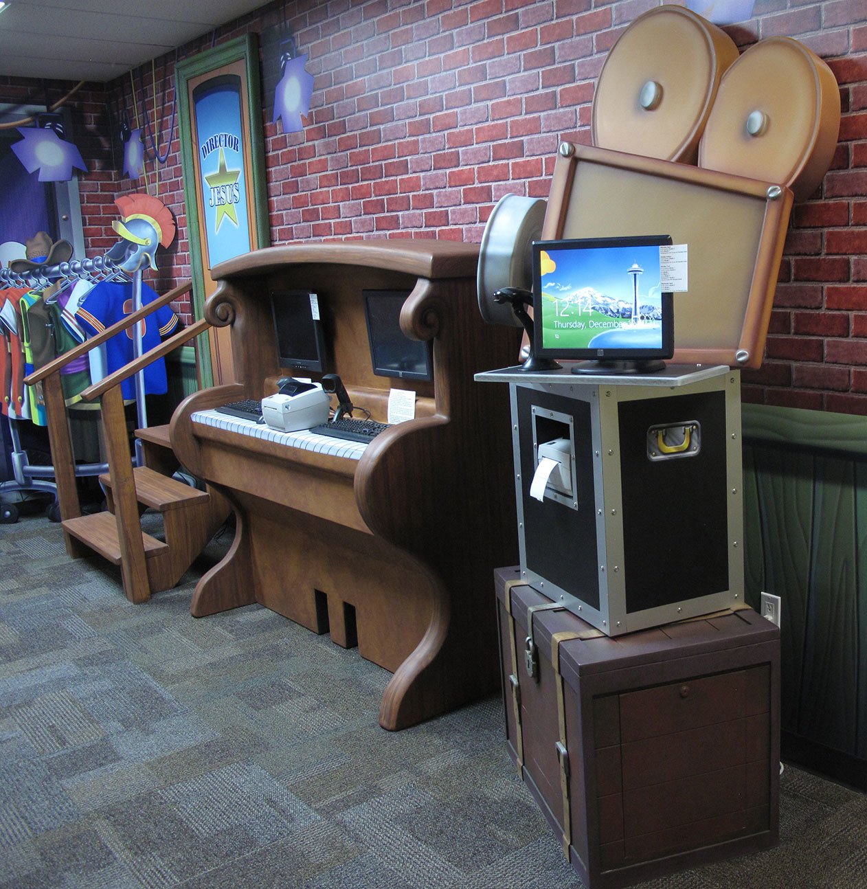 Backlot Studios Themed Space with Piano check in desk, road case, clothes rack and movie camera cutouts at Victory Church TX