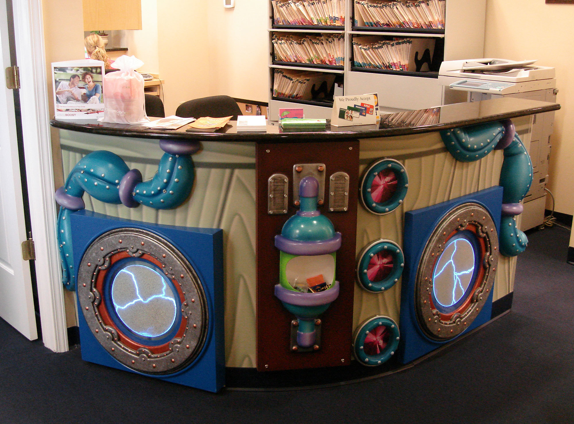 Science Lab Themed Check-In Desk with 3D relief sculpted plasma porthole windows, pipes, gas collectors and faux wood.