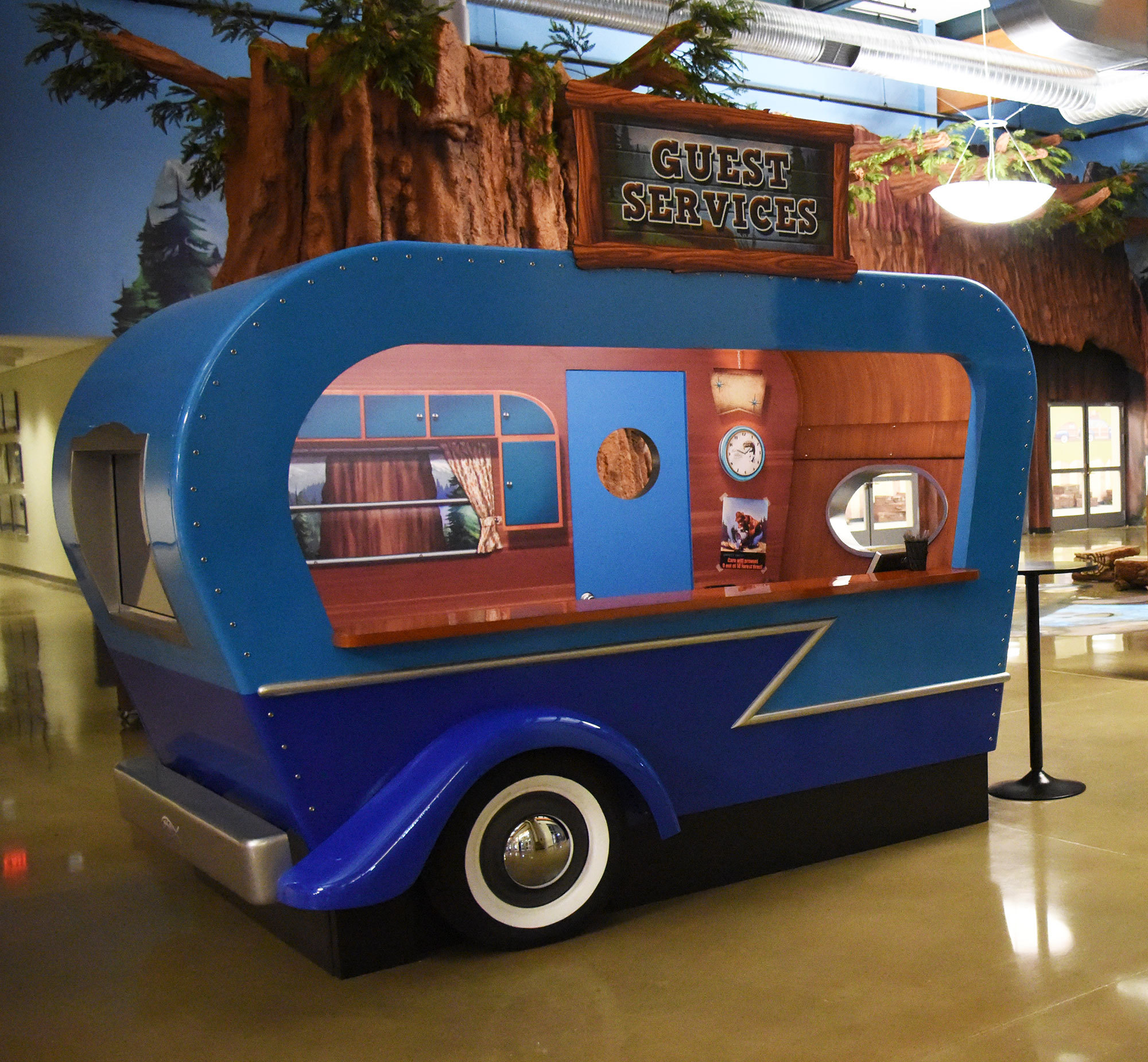 Blue/Wood 3D crafted vintage style Travel Trailer check in desk in a Camping Themed space.