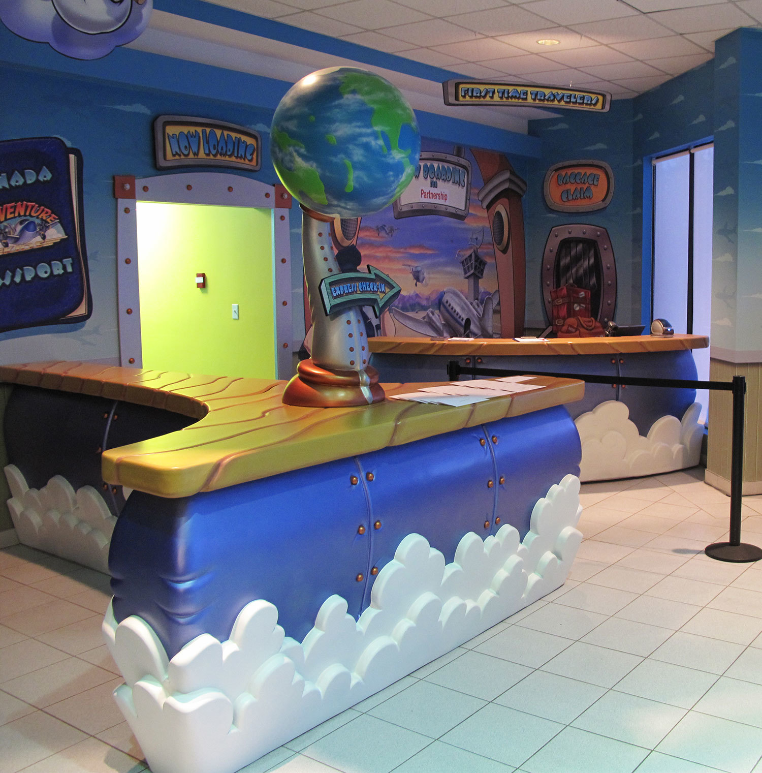 Airport Themed room with 3D sculpted Check-In Desk of sky and clouds with a carved faux wood countertop and airport scene murals behind.