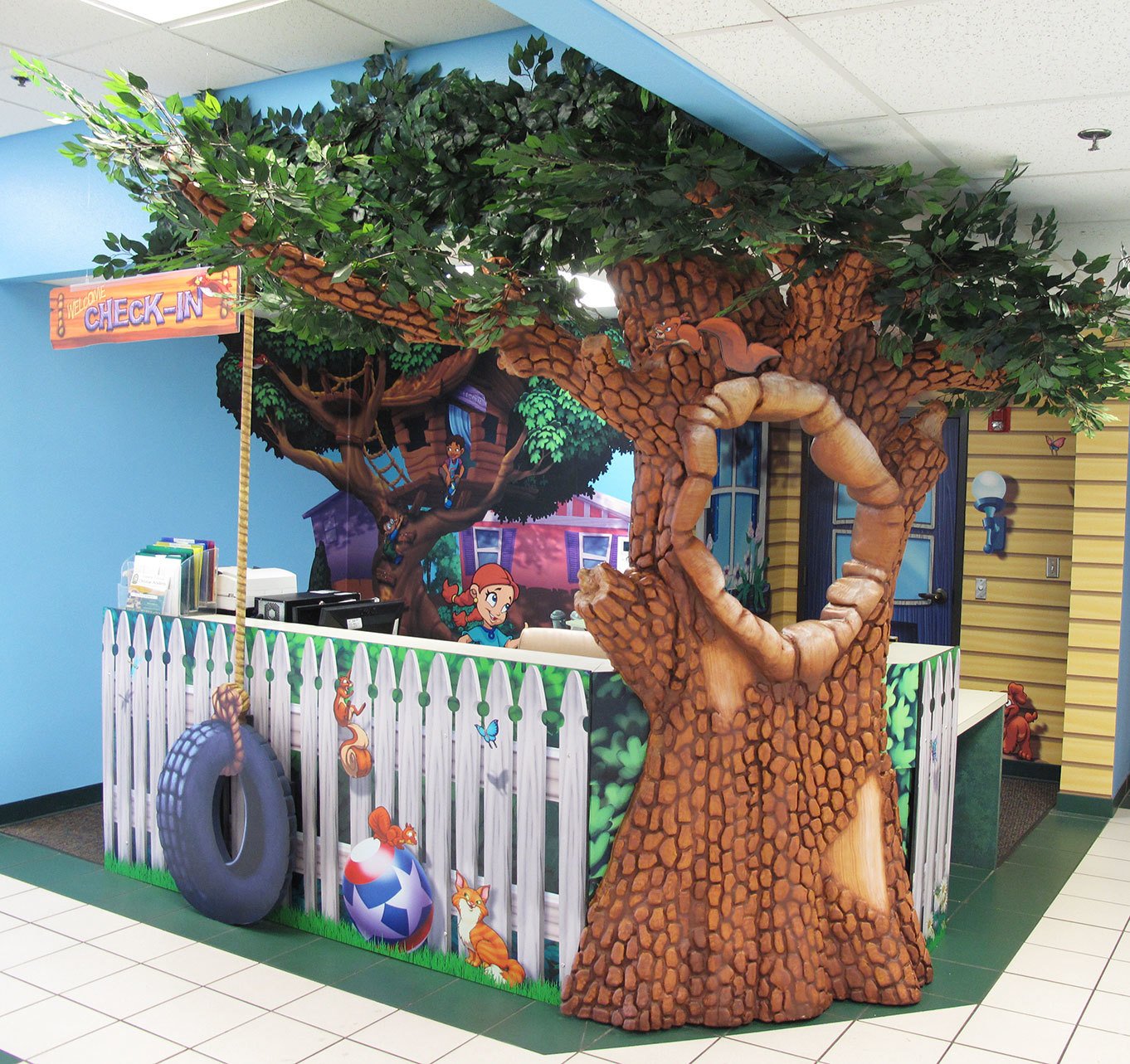 Neighborhood Themed Check-In Desk with 3D sculpted tree with tire swing and white picket fence desk wrap