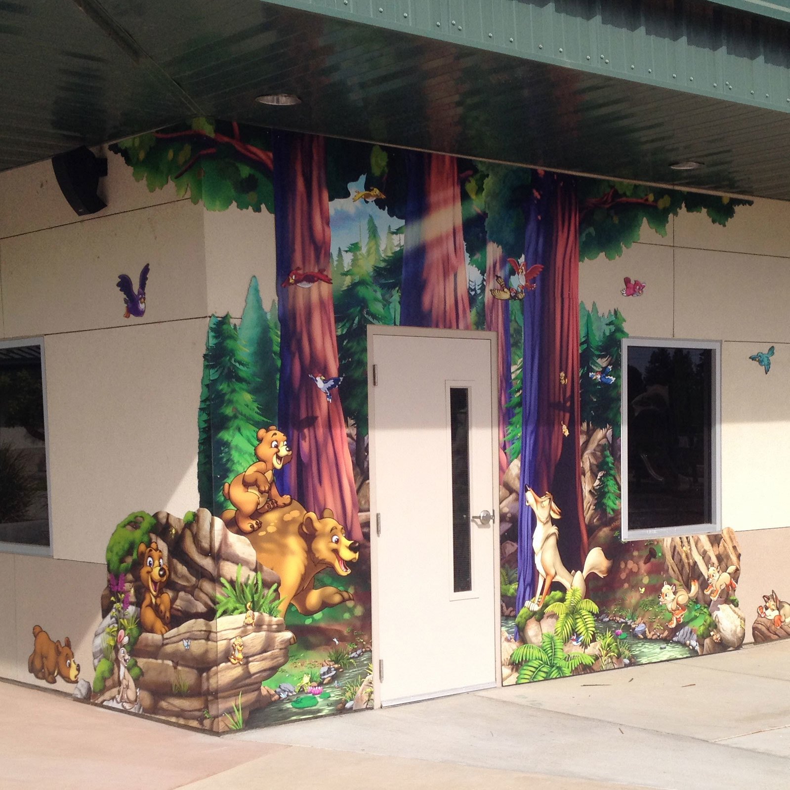 Outdoor contour cut mural depicting a forest scene with bears, wolves and birds surrounding a doorway of a church