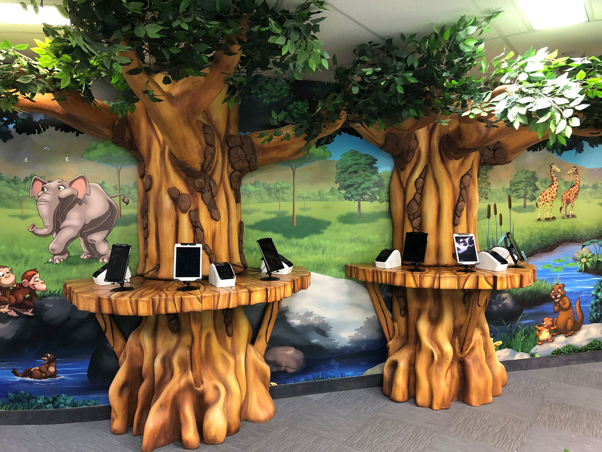 3D Sculpted Tree Check In Kiosk Stations with wall murals depicting an African plain with Giraffes, elephants and monkeys.